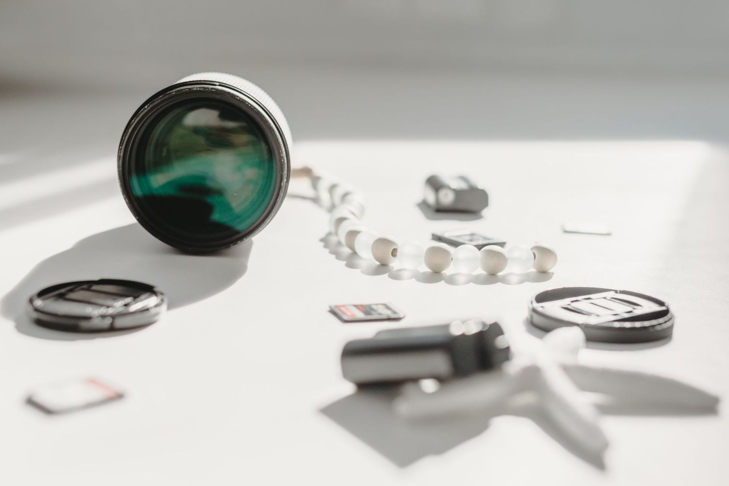 Camera lens, memory cards, lens caps and photography accessories scattered on white surface.
