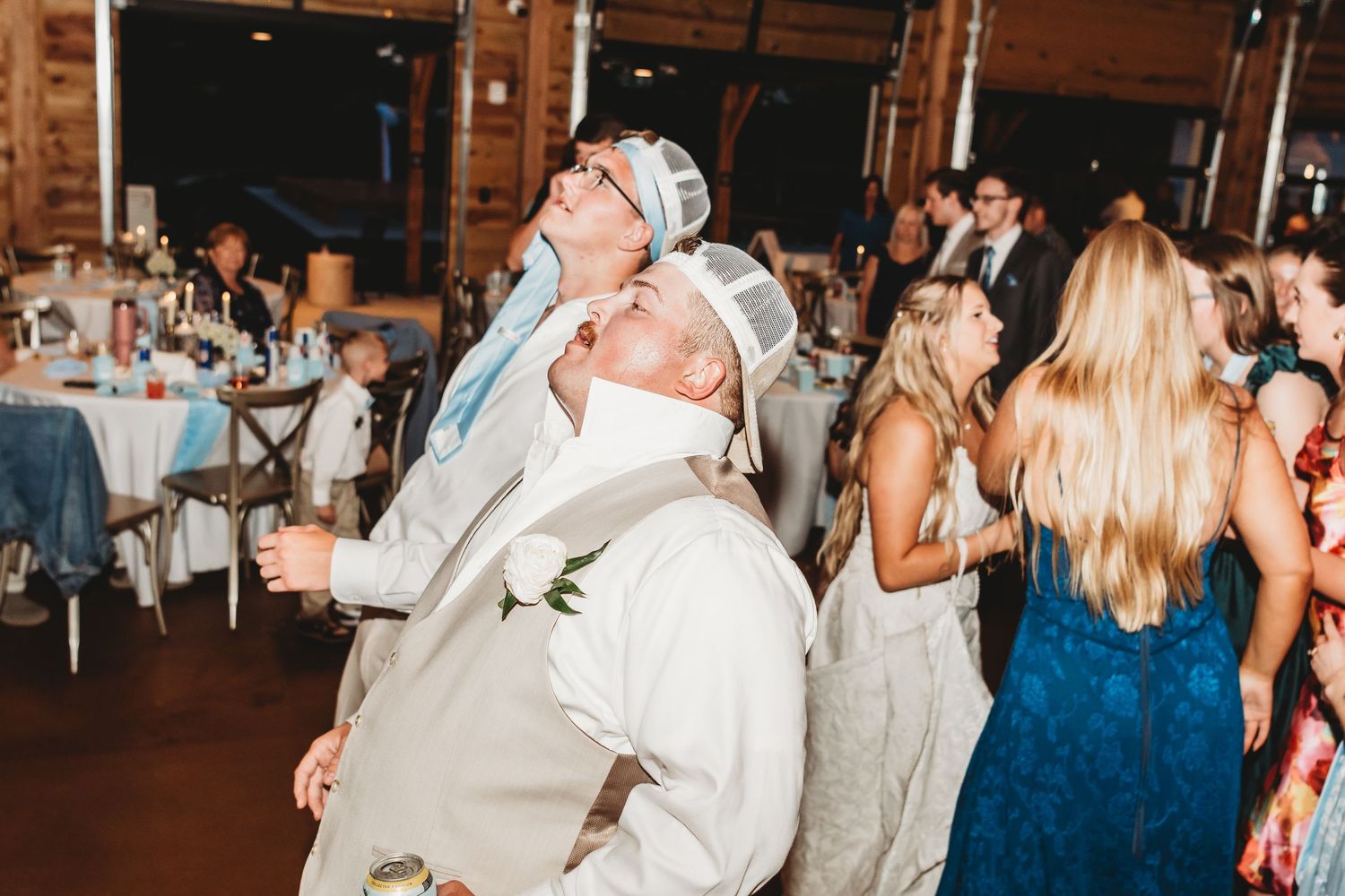 Groomsmen in tan suits dancing energetically at a lively indoor wedding reception celebration.