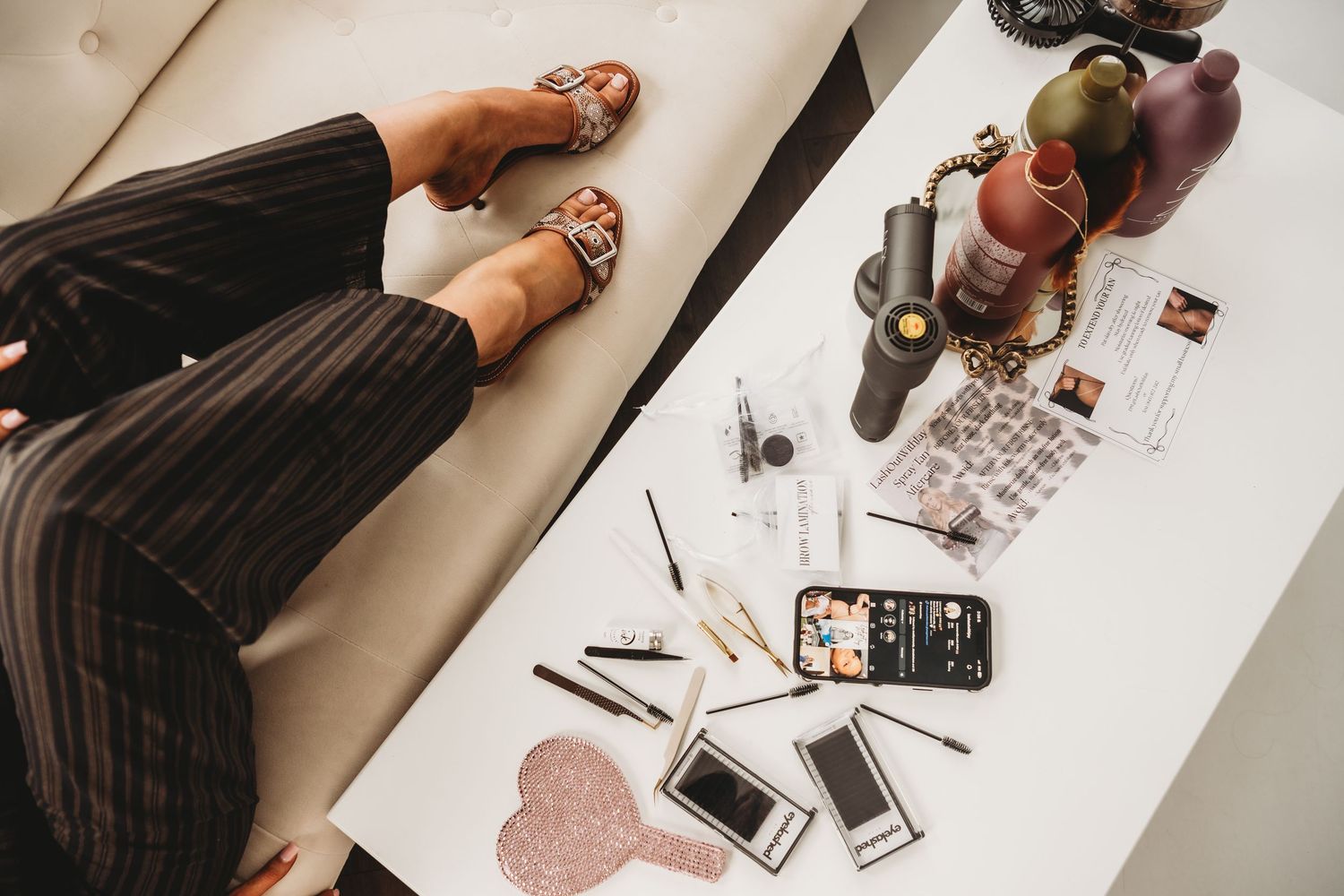 Overhead view of makeup tools, phones, and accessories on white table.