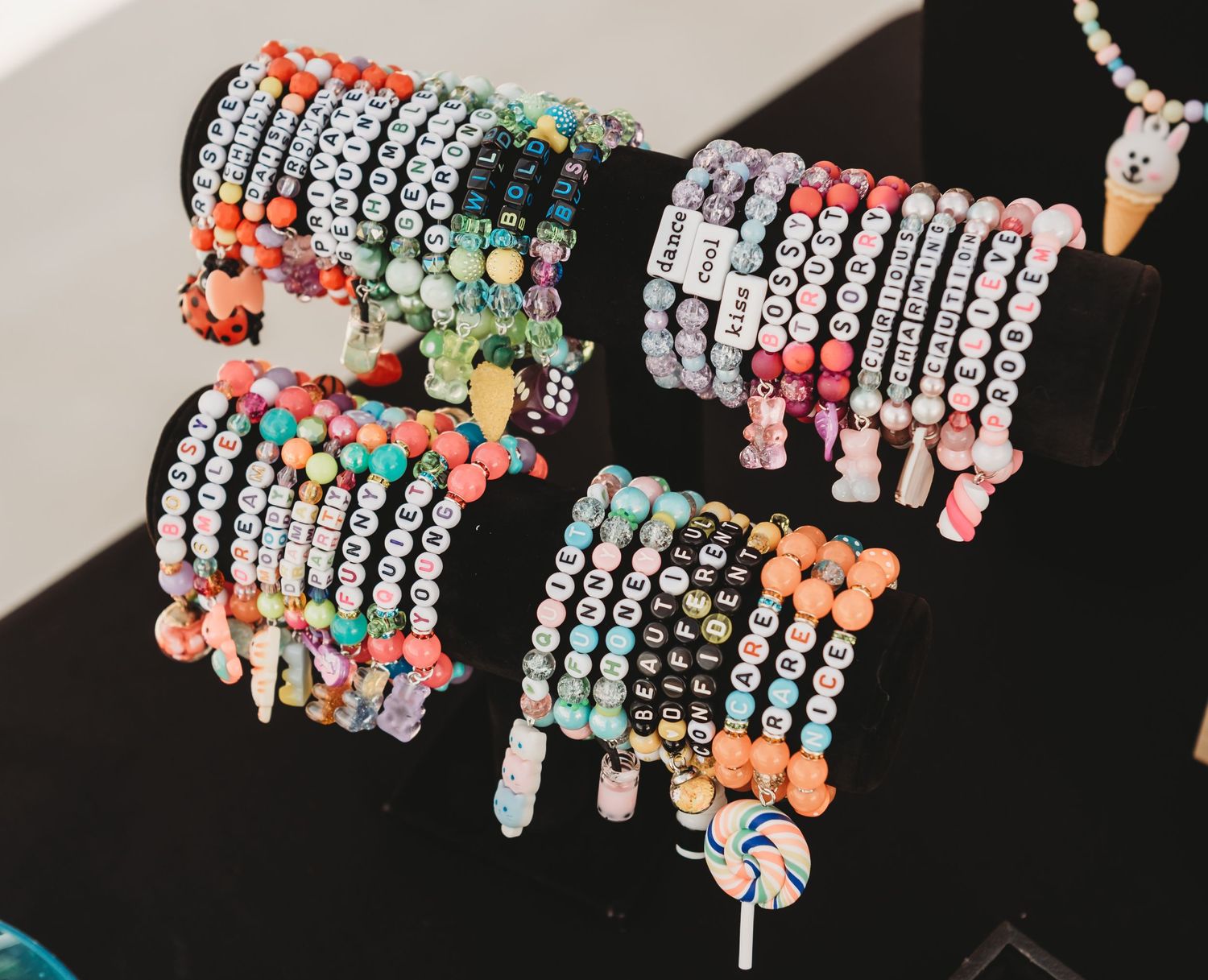 Colorful beaded bracelets with letter charms displayed on black bracelet stands at a jewelry market.