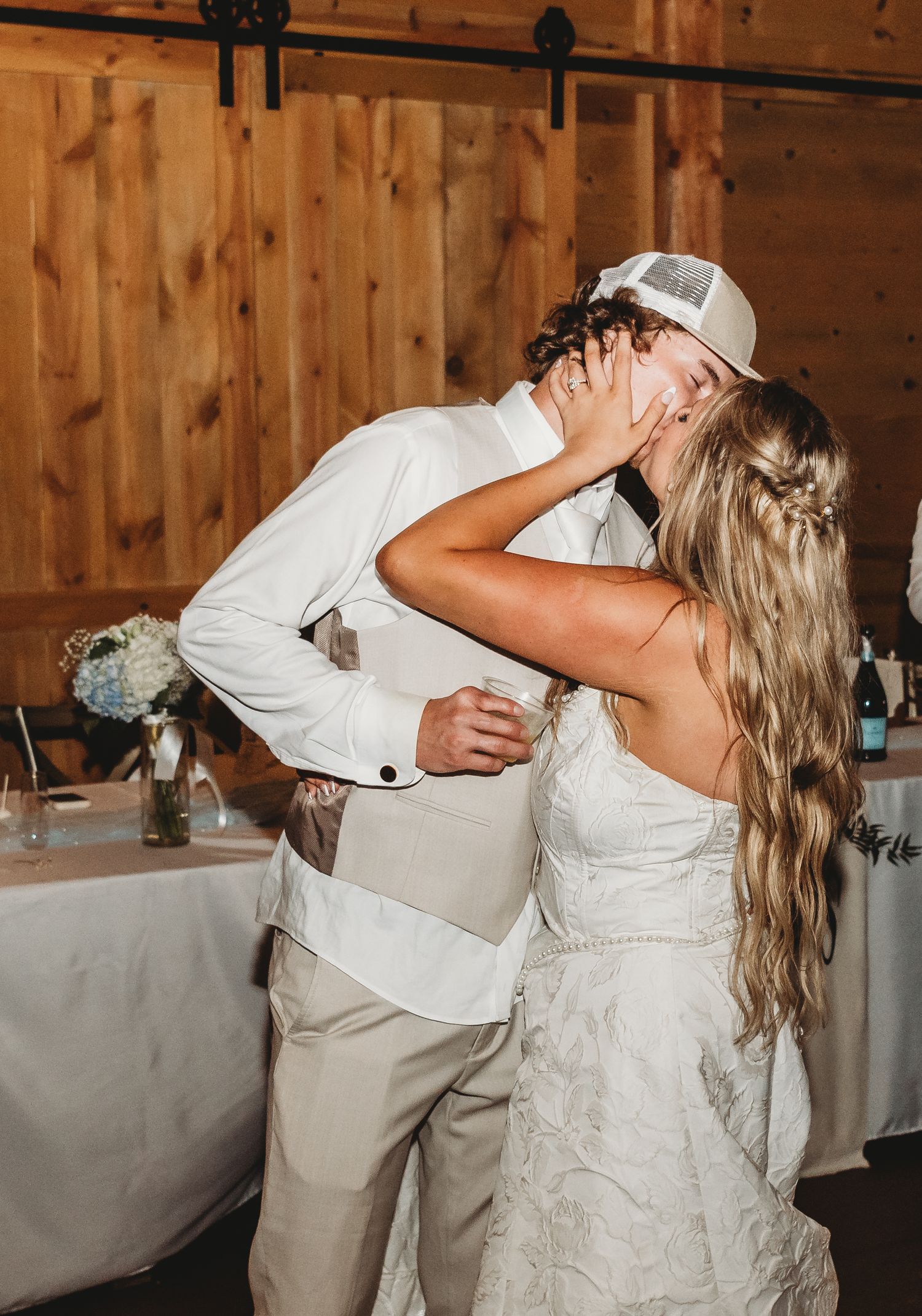 Bride and groom sharing romantic kiss in rustic barn wedding venue with wood walls.