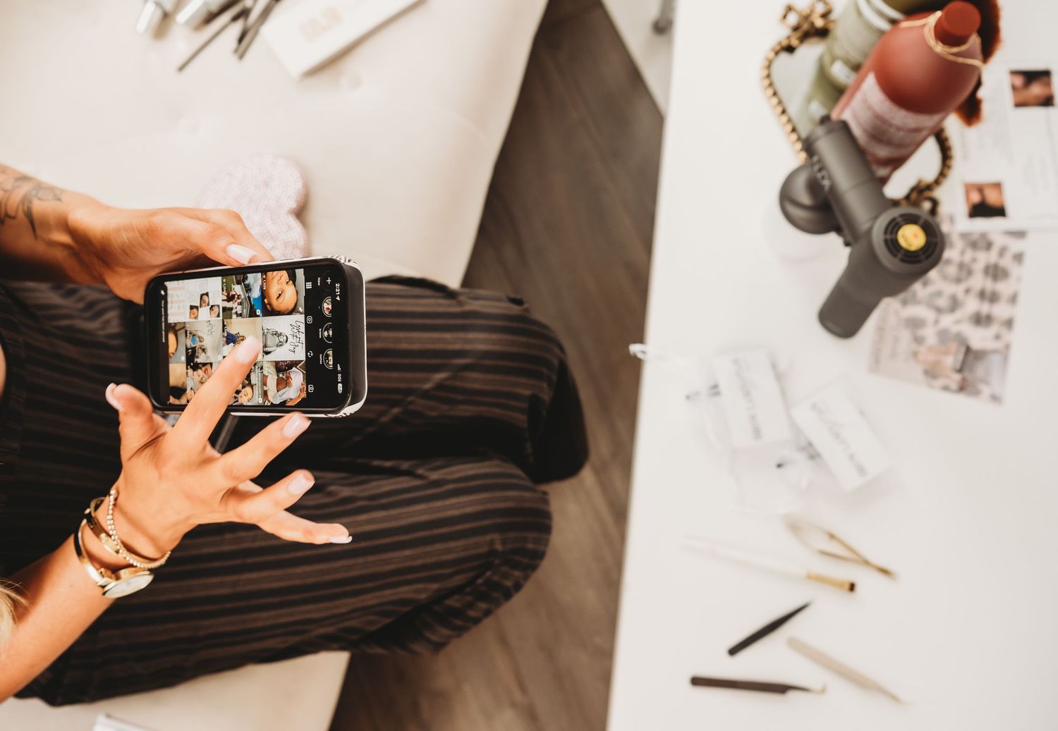 Overhead view of woman photographing beauty products with smartphone at desk.