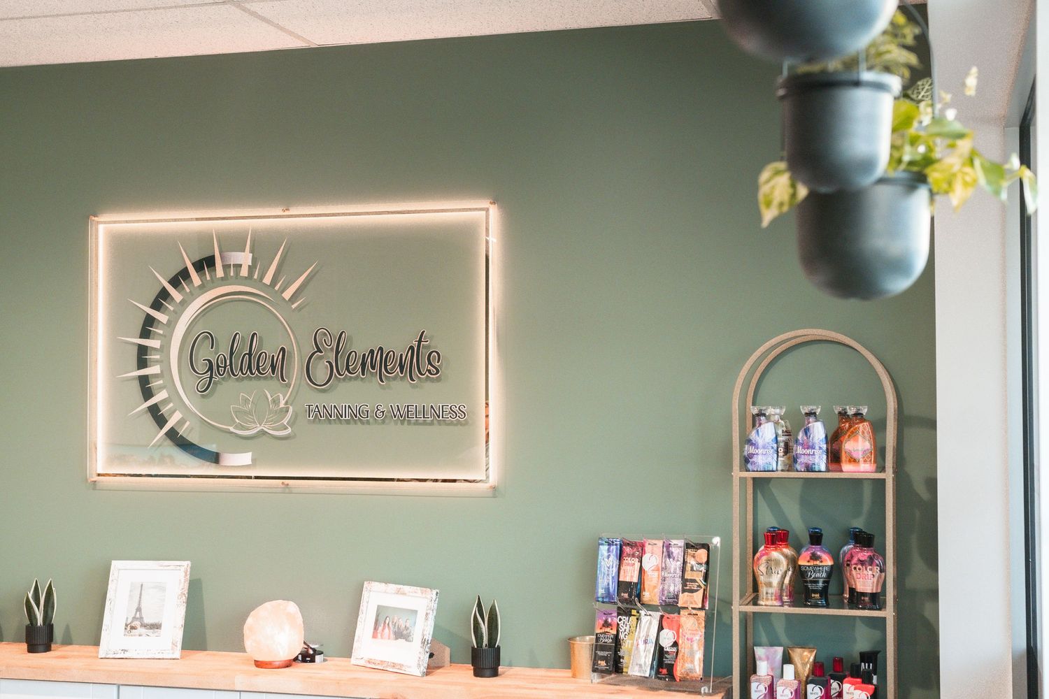 Golden Elements spa reception desk with green accent wall, illuminated logo sign, and retail product display.