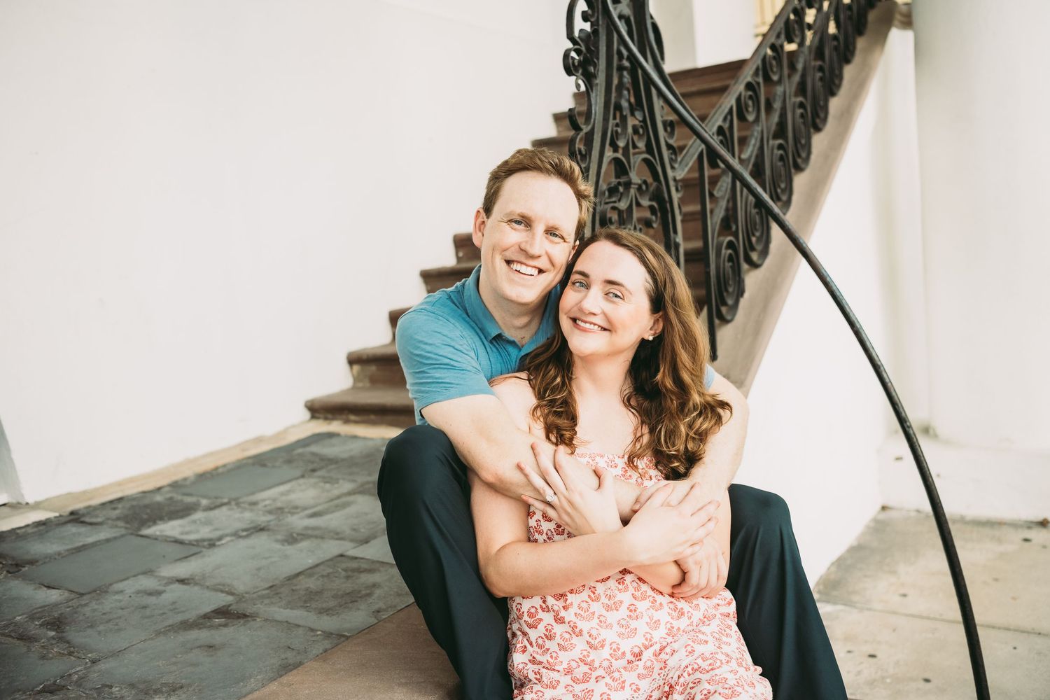 Happy couple sitting on stairs embracing and smiling during engagement photo session.
