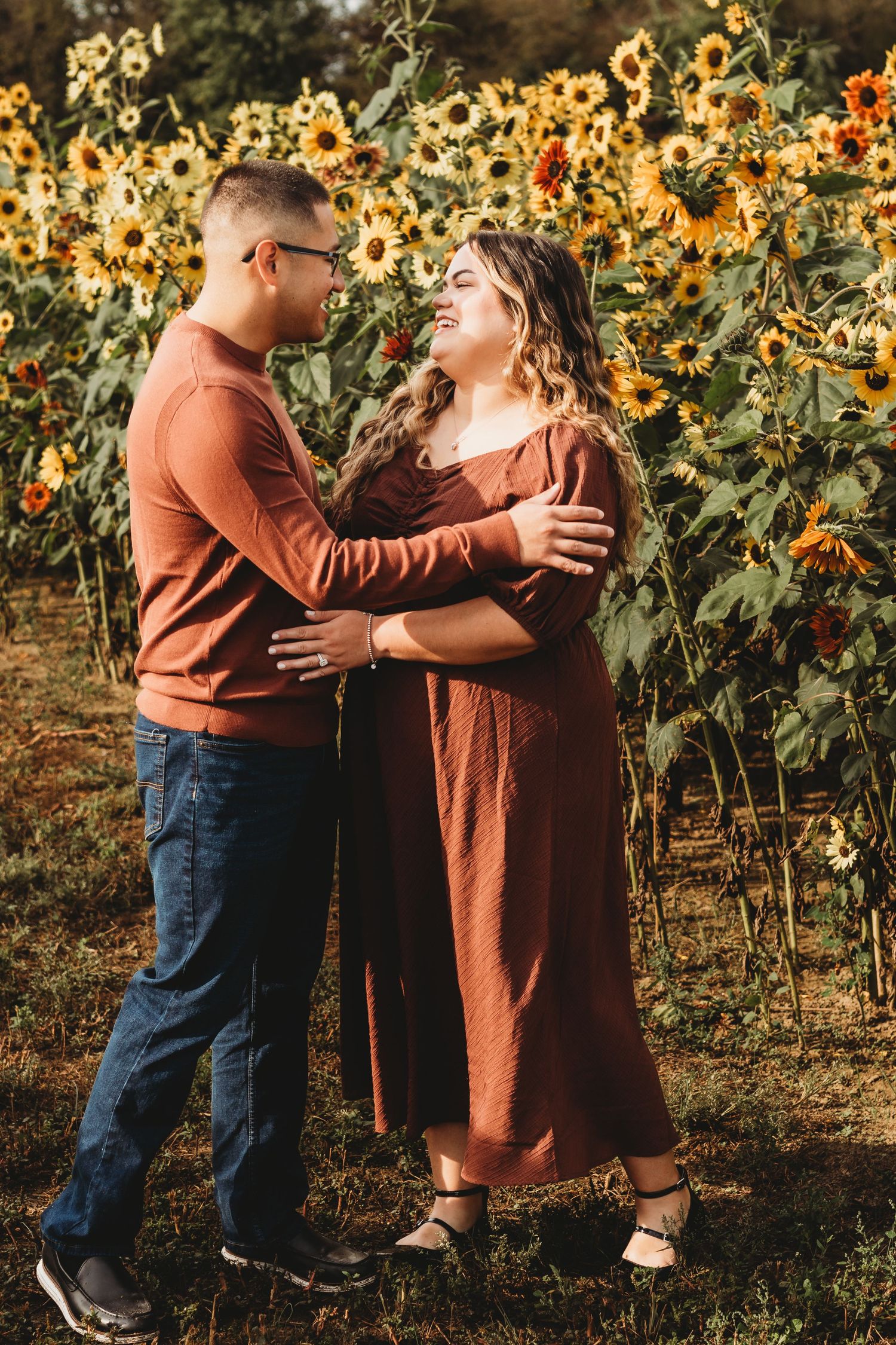 Couple embraces lovingly in front of a vibrant sunflower field on a warm autumn day.