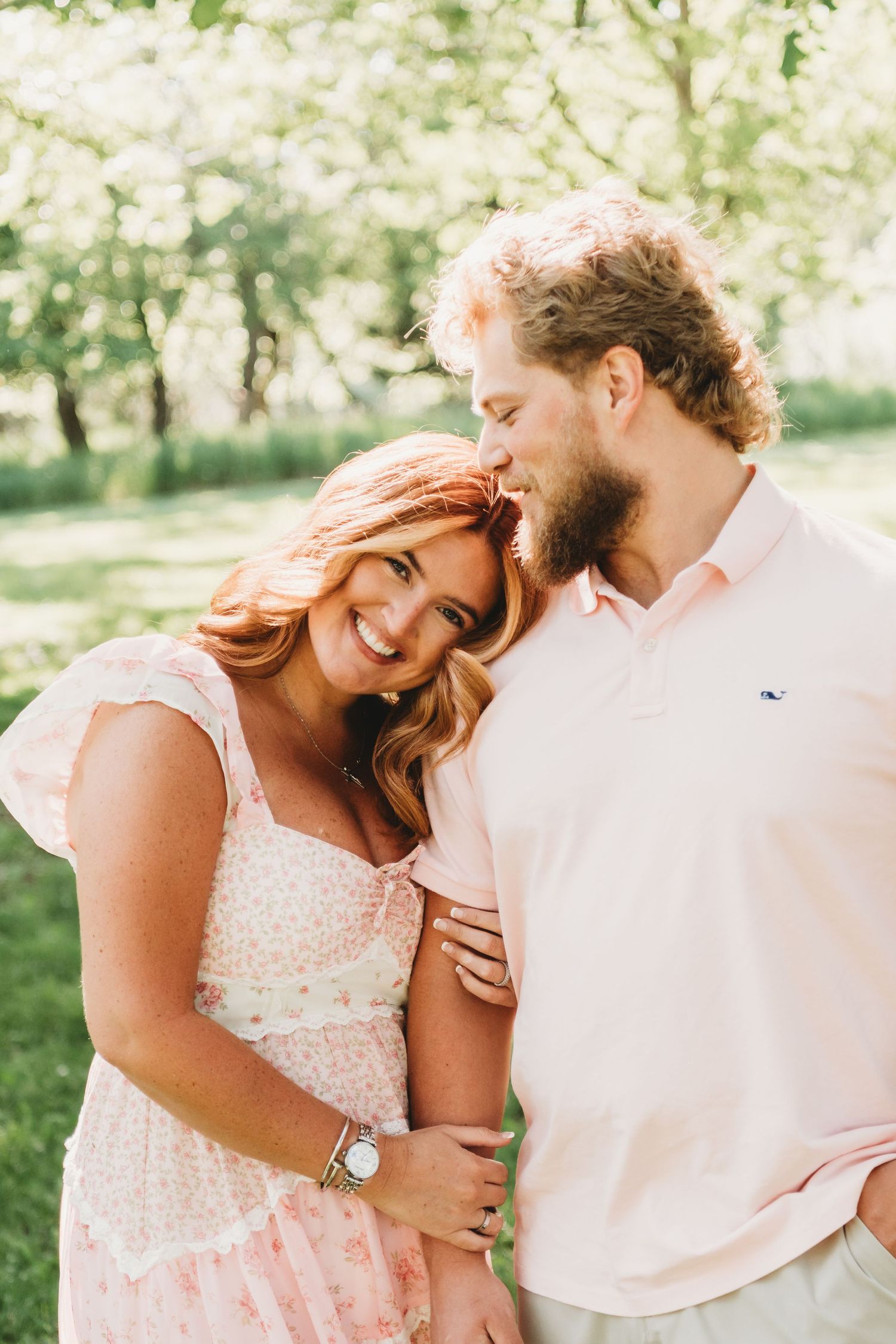 Couple sharing a tender moment in a sunlit orchard, woman smiling as man kisses her head.