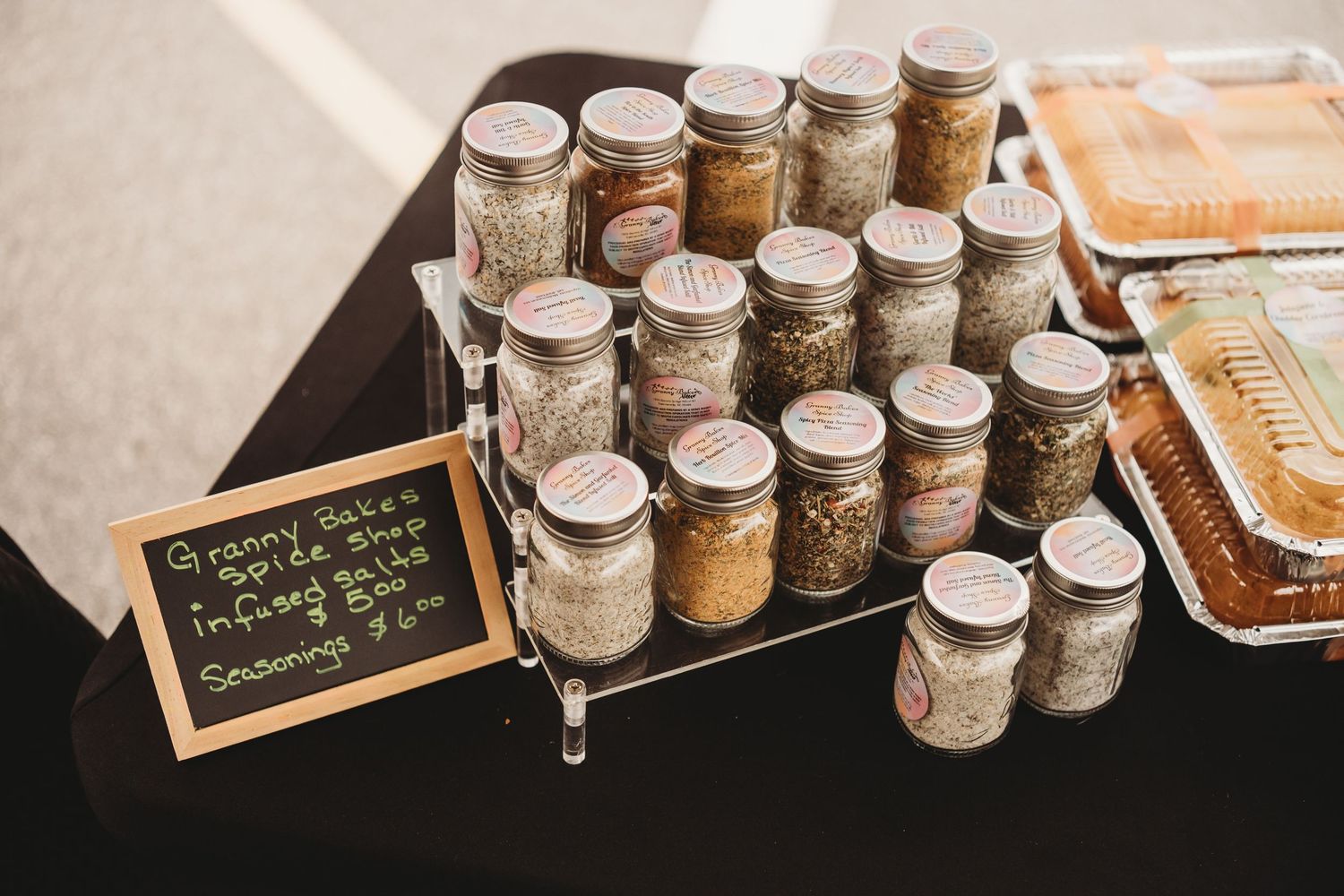 Mason jars filled with homemade spice seasonings displayed on a tiered rack at a farmers market booth.