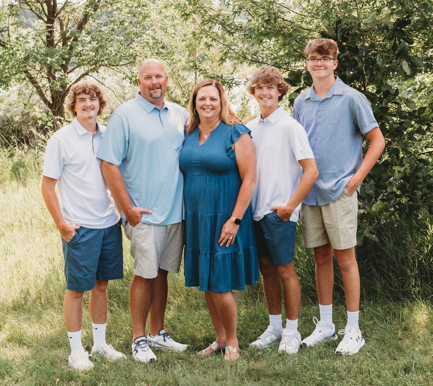 A family of five smiles together outdoors wearing coordinated blue and white outfits in summer.