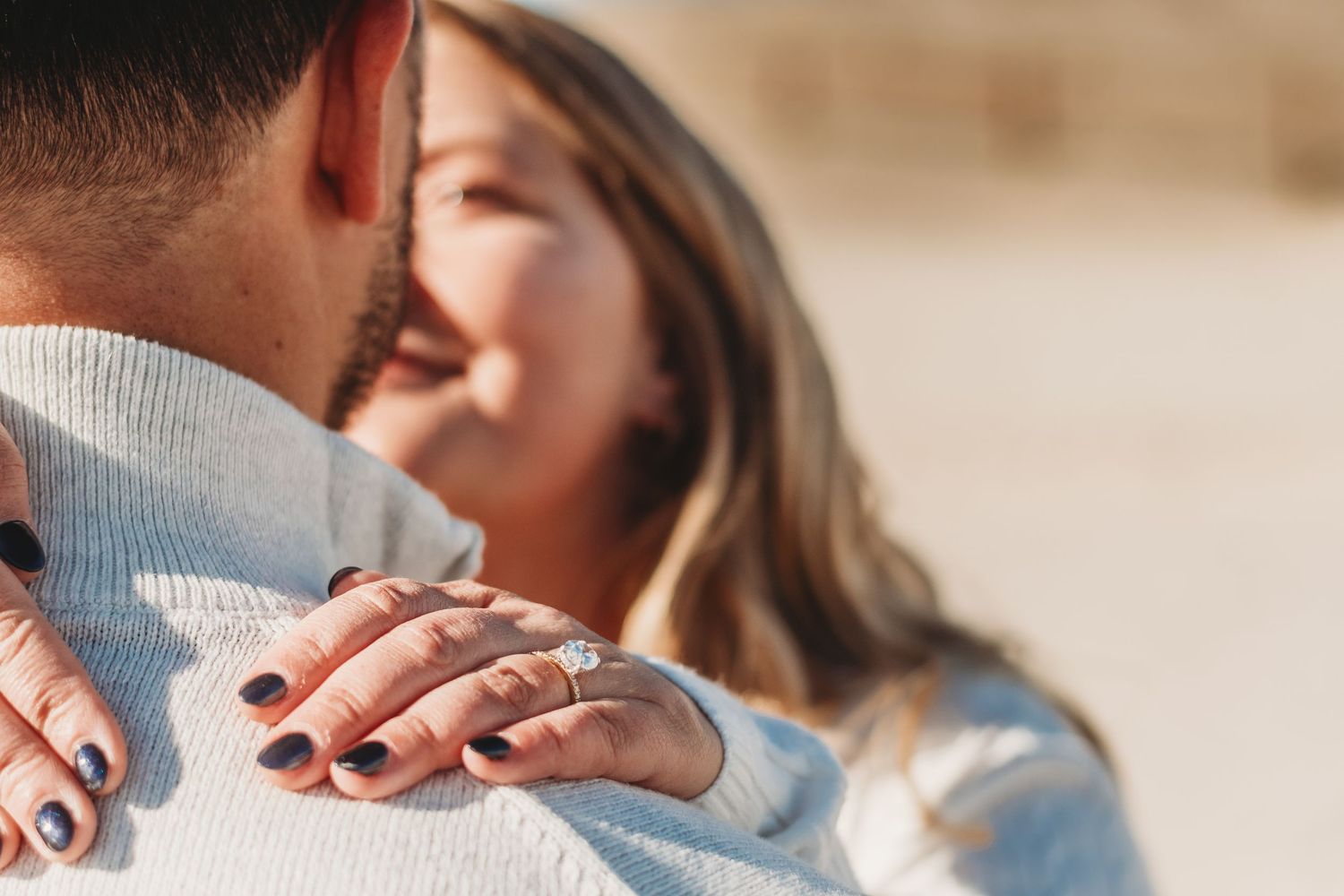 Close-up of engagement ring on woman's hand while embracing partner.