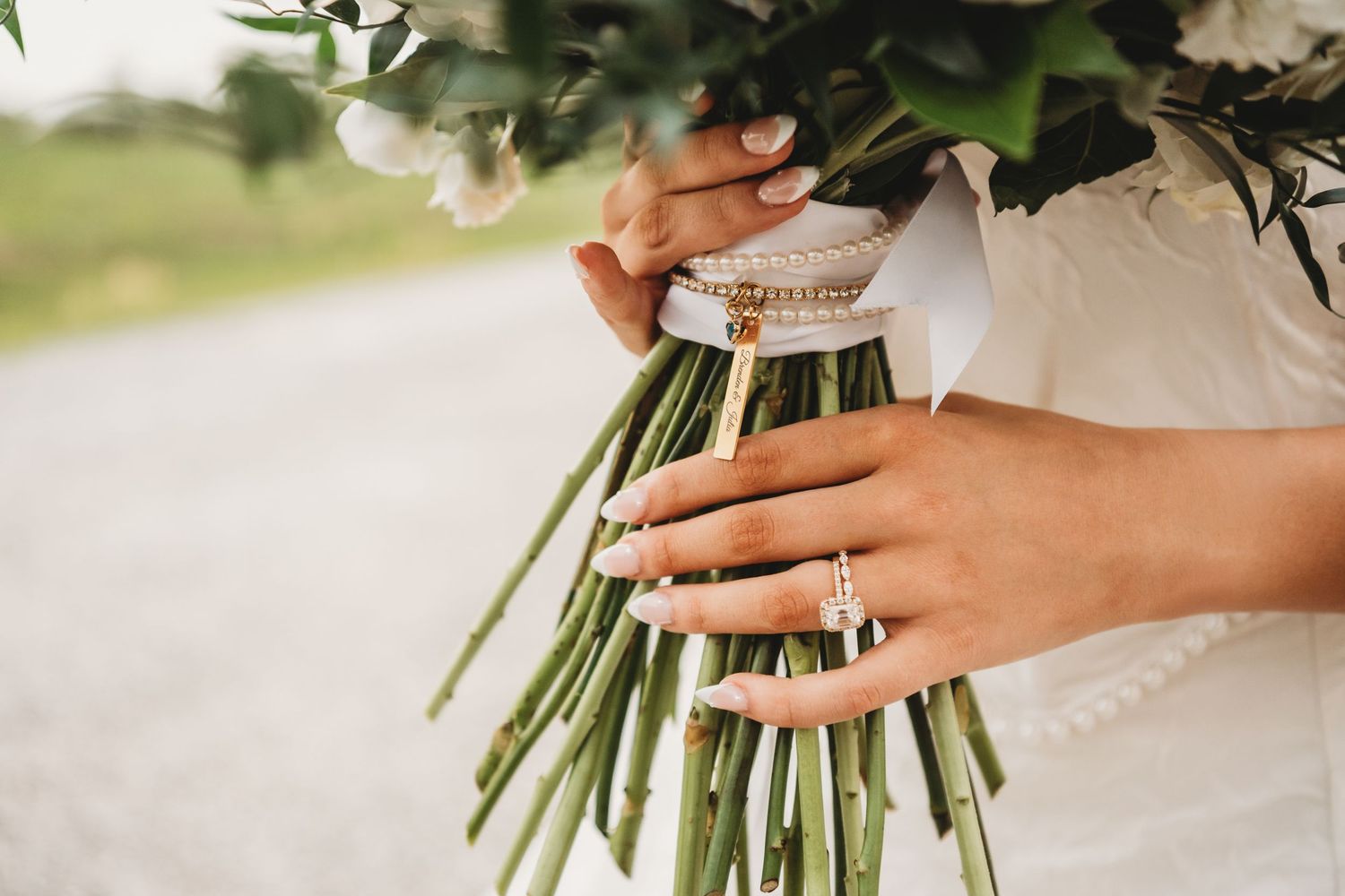 Close-up of bride's hands holding white flower bouquet with gold bracelet and diamond wedding ring.