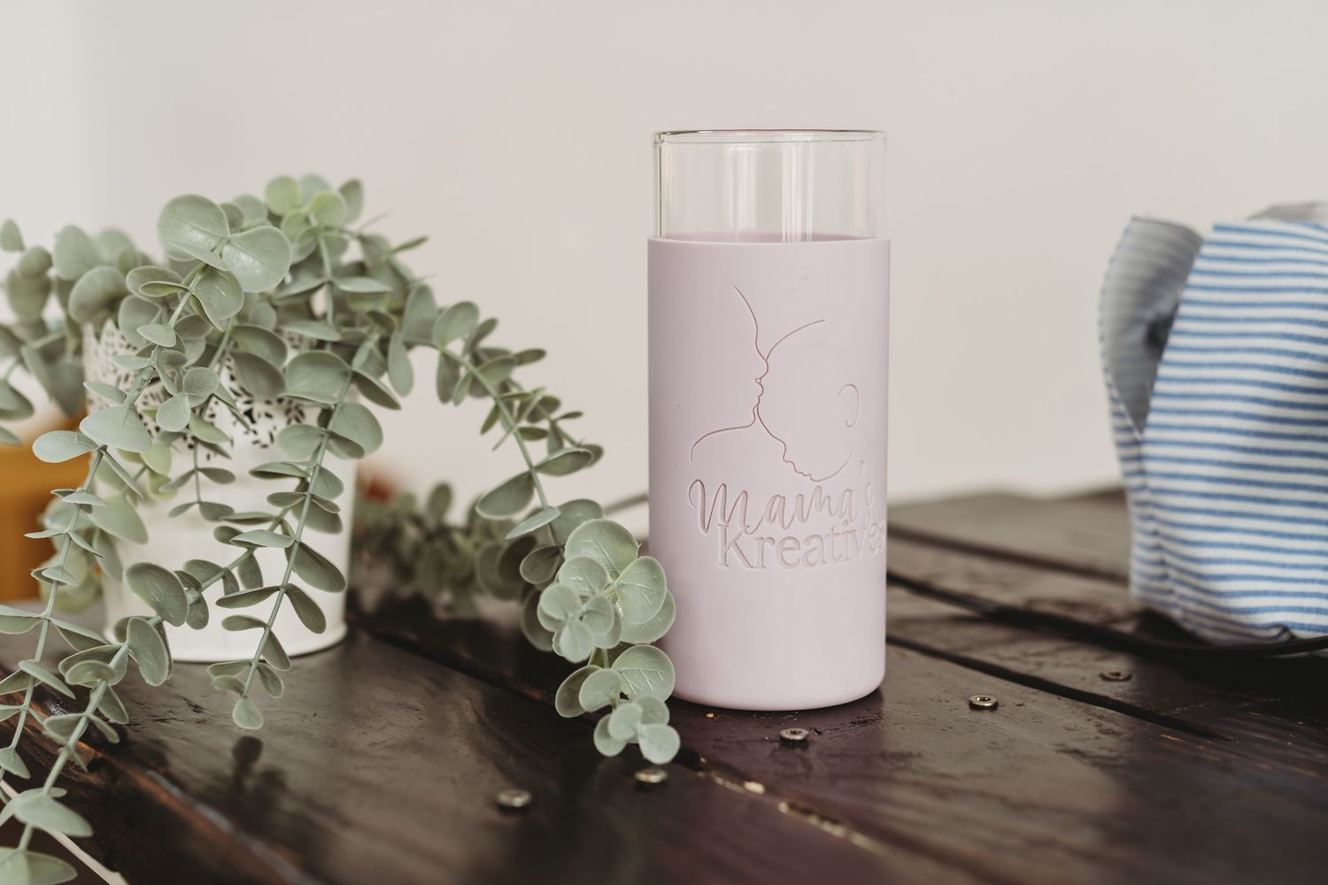 Pink Milky Kreams branded tumbler with glass top on dark wood table with eucalyptus branches.