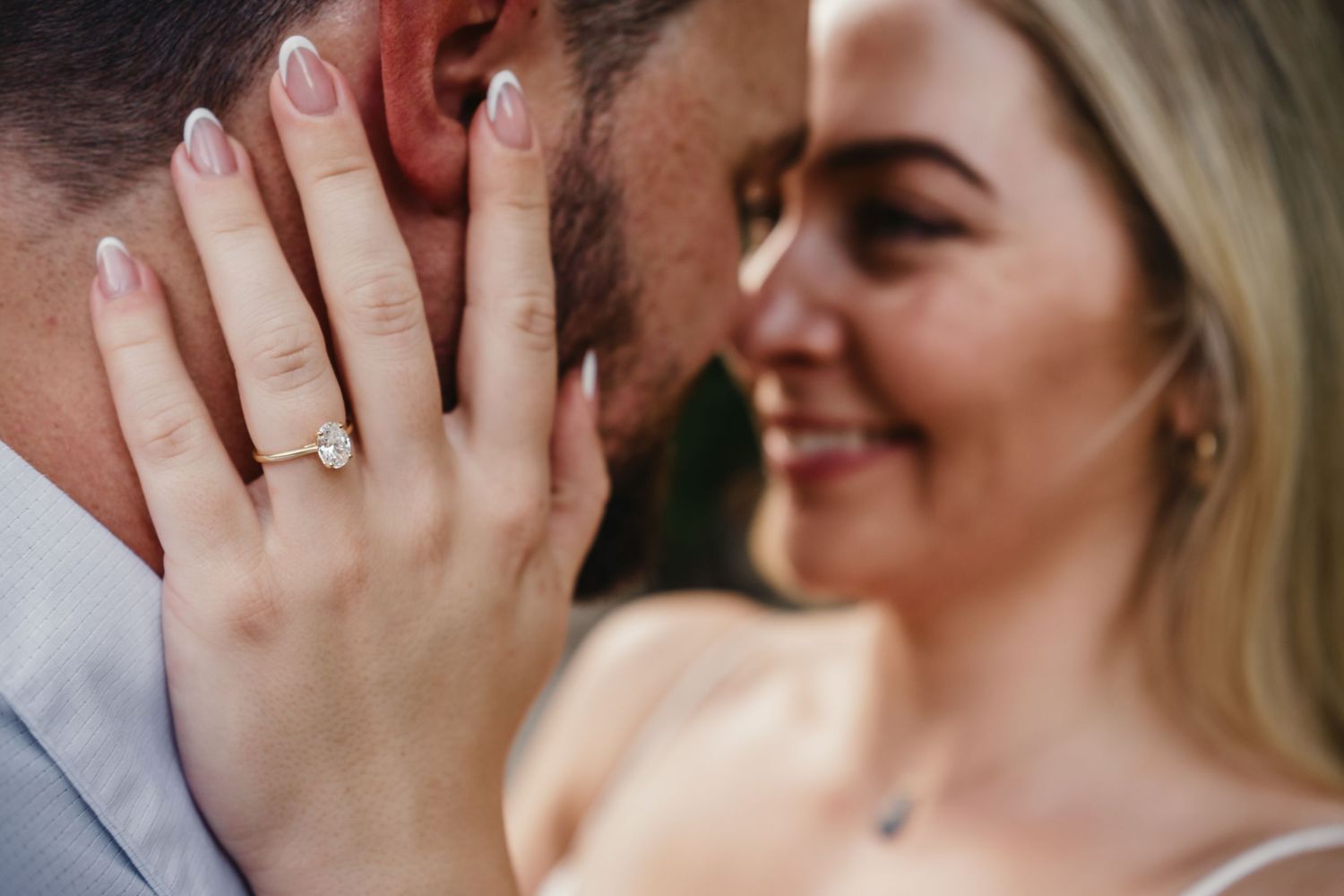 Close-up of woman smiling with engagement ring on hand gently touching mans face during romantic moment.