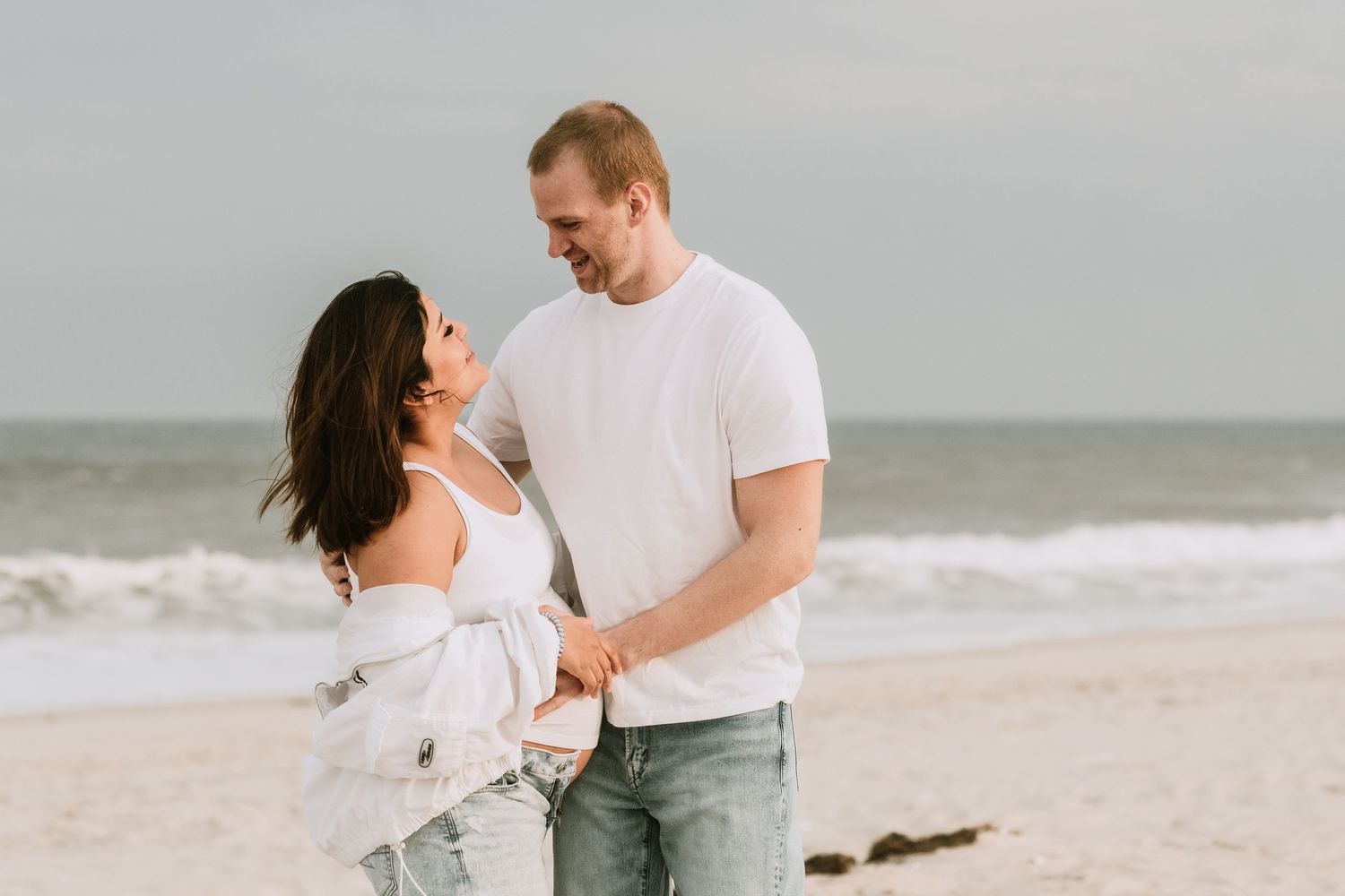 Happy couple holding hands and smiling at each other on a beautiful sandy ocean beach.
