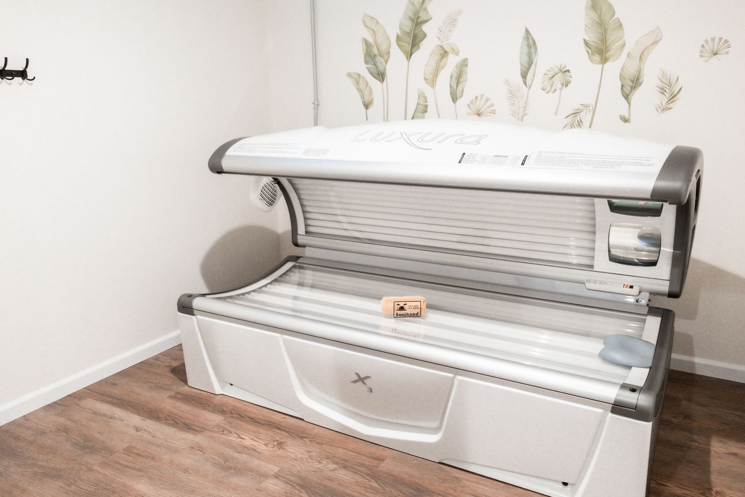 Modern tanning bed in a clean, white spa room with floral wall decor and hardwood floors.