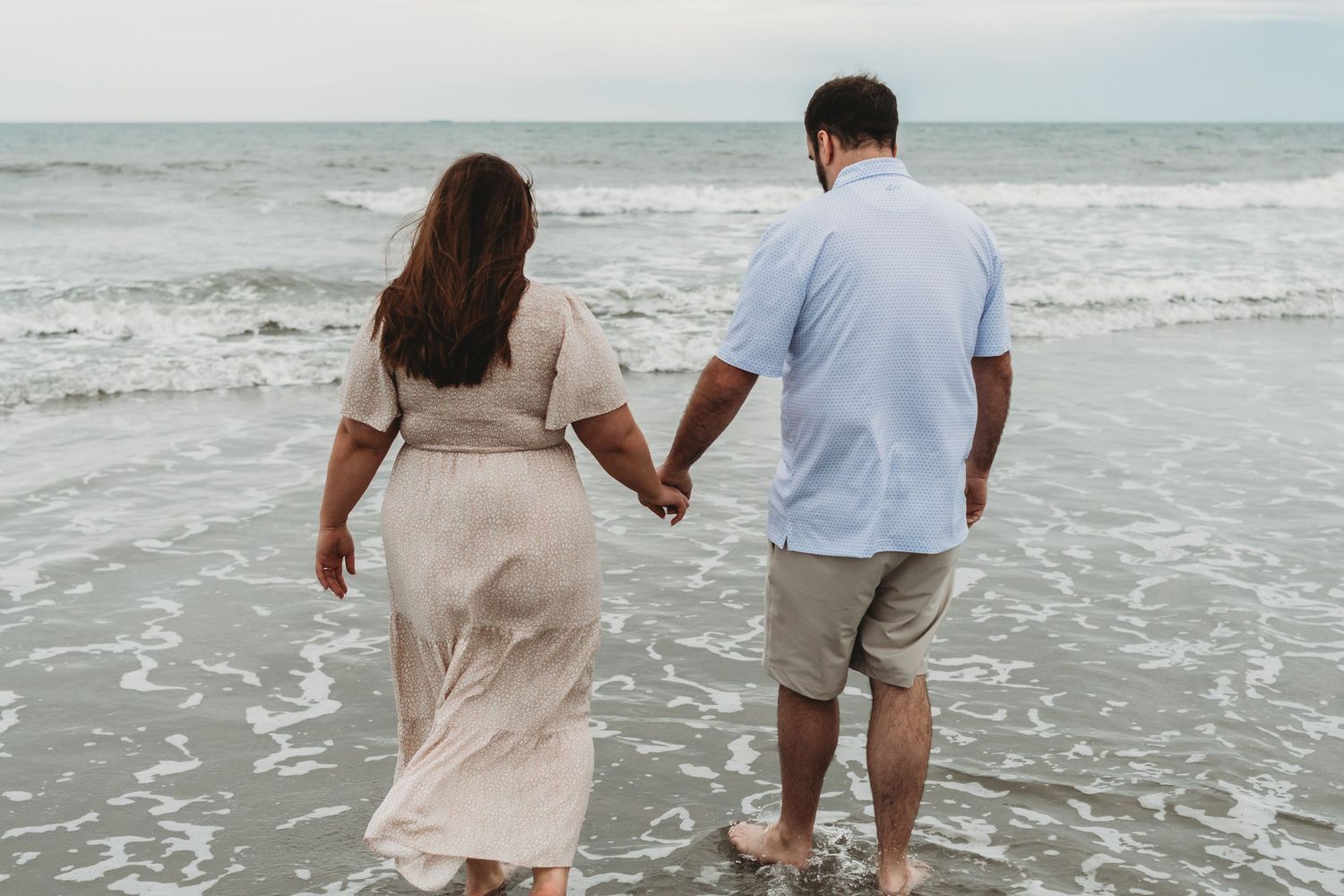 Couple holding hands walking along ocean shoreline at beach.