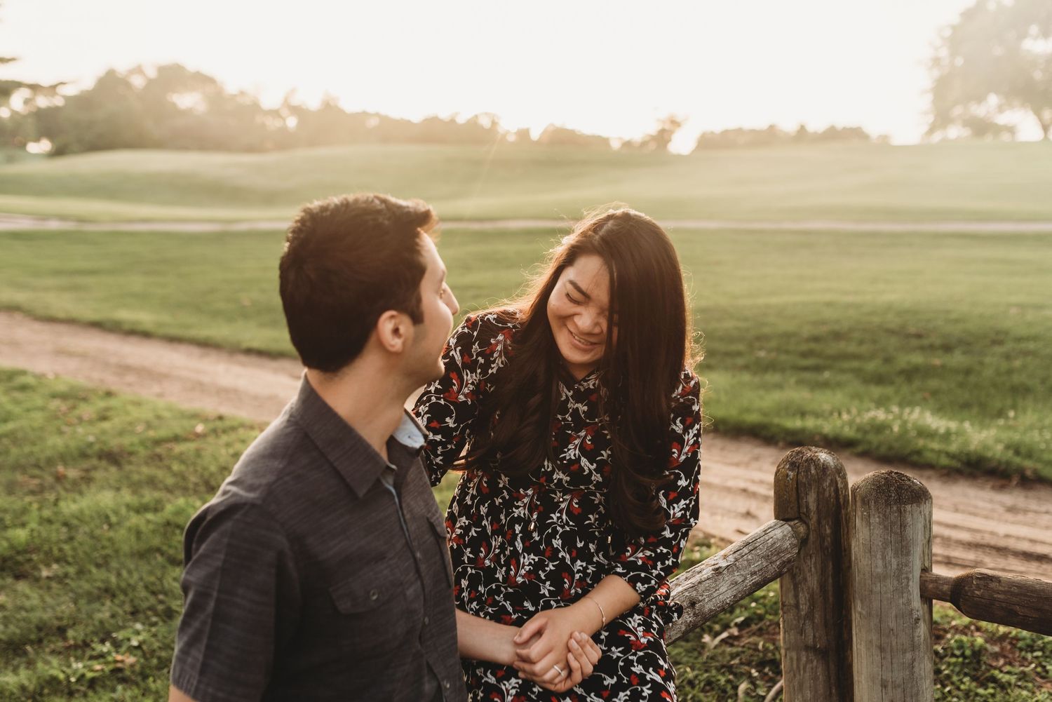 Couple holding hands and smiling at sunset by rustic wooden fence.