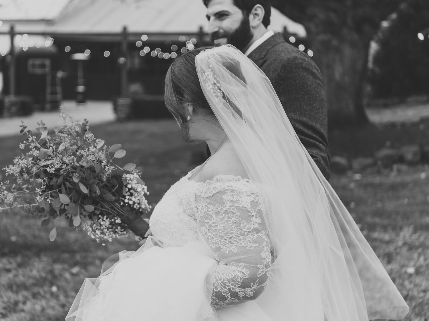 Black and white photo of bride and groom embracing outdoors near rustic barn venue.