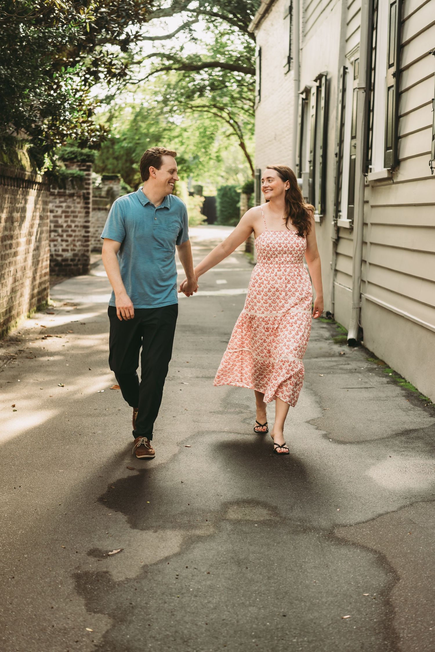 Joyful couple holding hands and walking together down a charming tree-lined alley in summer.