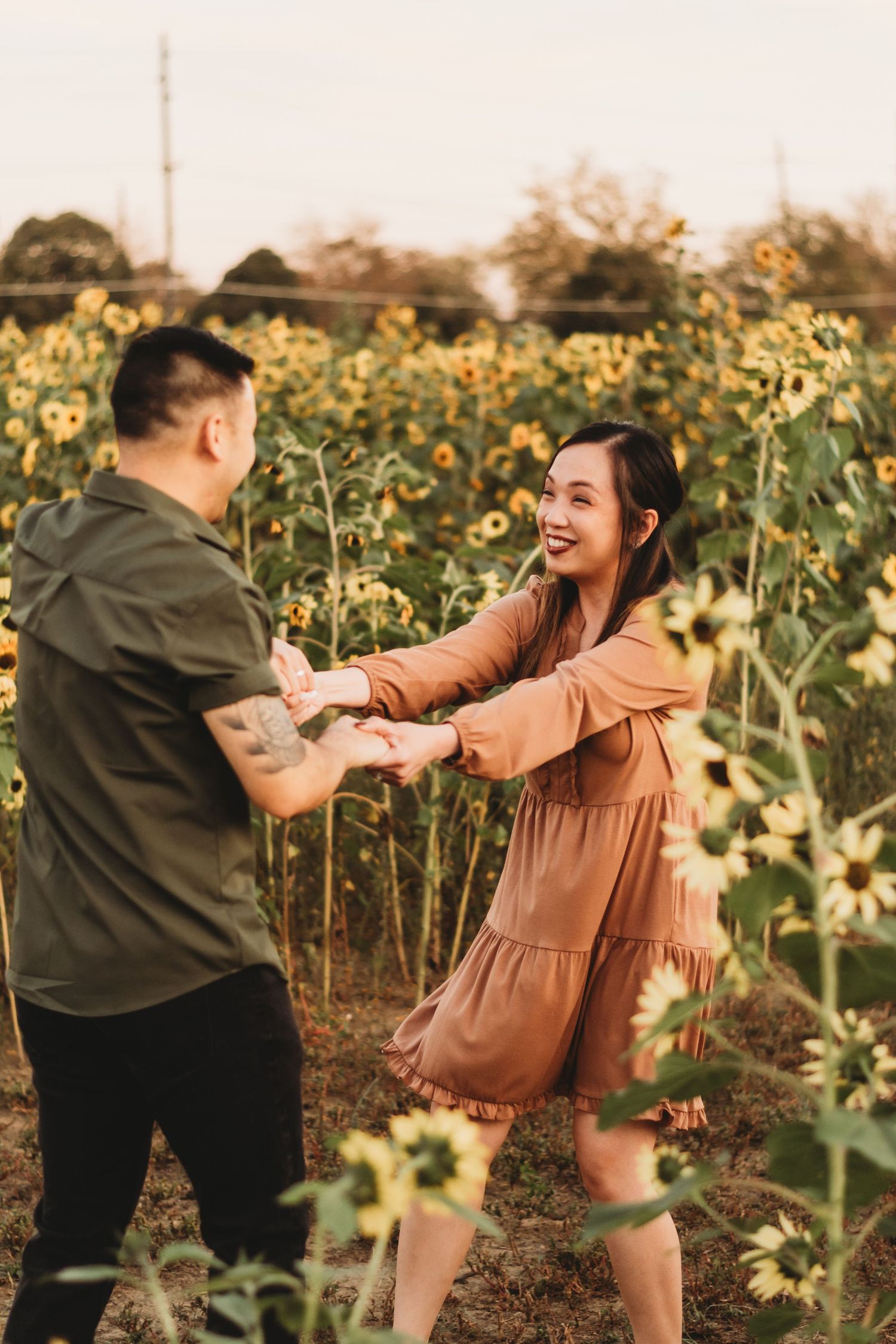 Smiling woman in brown dress holding hands with man in sunflower field.