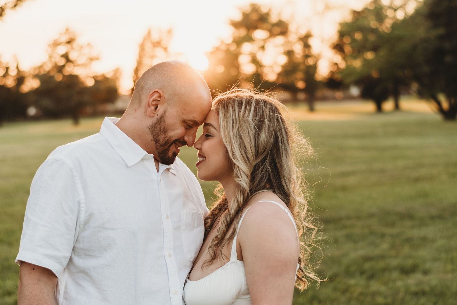 Couple touching foreheads in tender moment during golden hour sunset in green park setting.