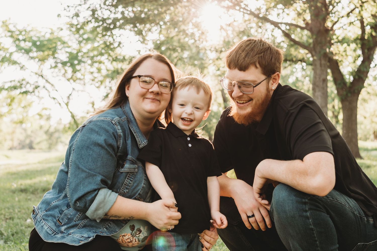 Happy family of three smiling outdoors in a sunny green park during a family portrait session.