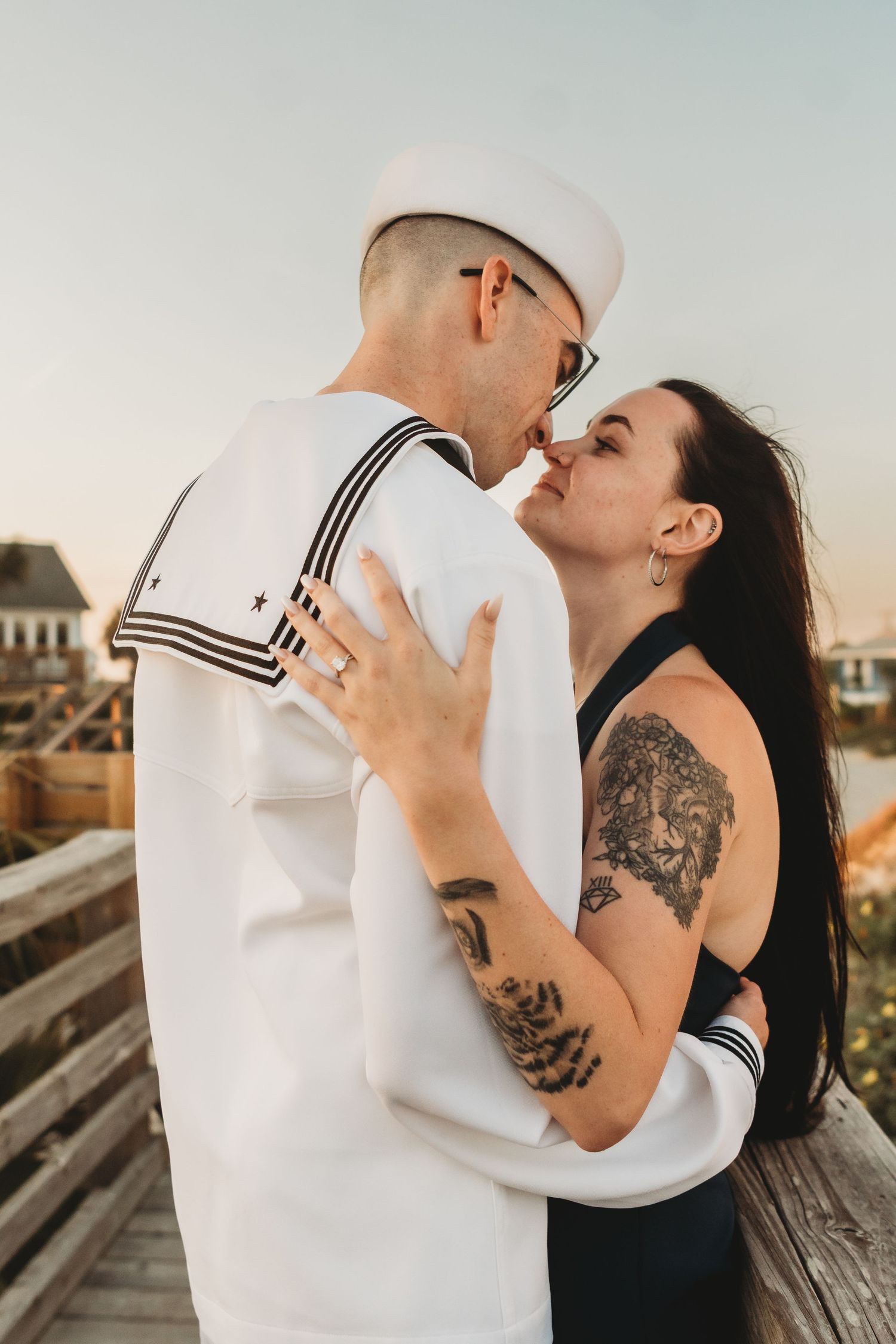 Couple sharing romantic moment on boardwalk at sunset, man in navy sailor uniform.