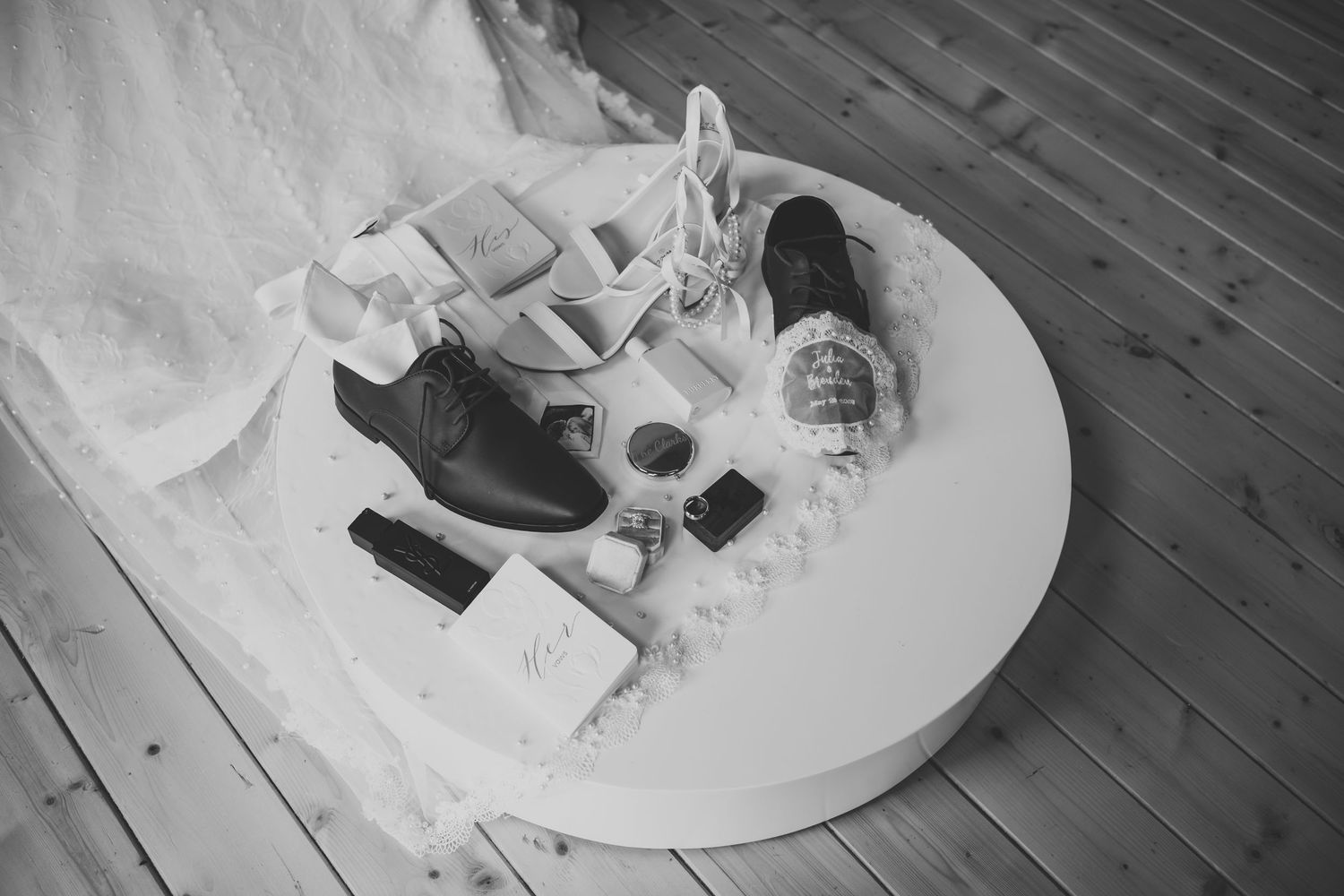 Black and white flat lay of wedding shoes and accessories on round table.