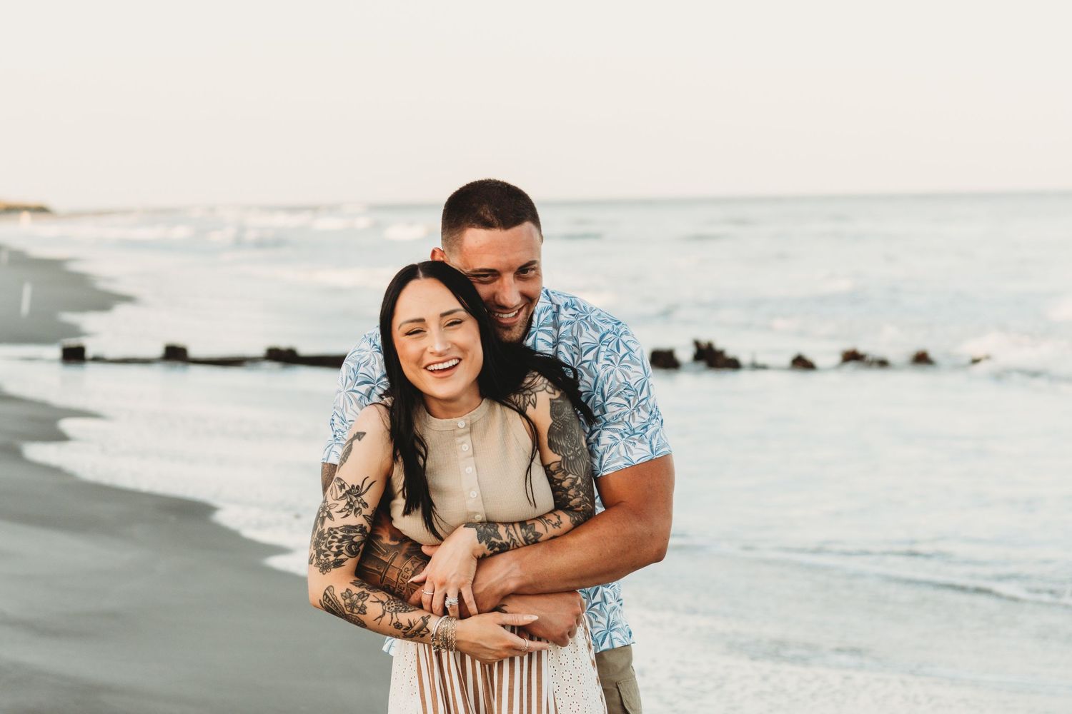 Happy couple embracing and laughing together on a scenic ocean beach at sunset.