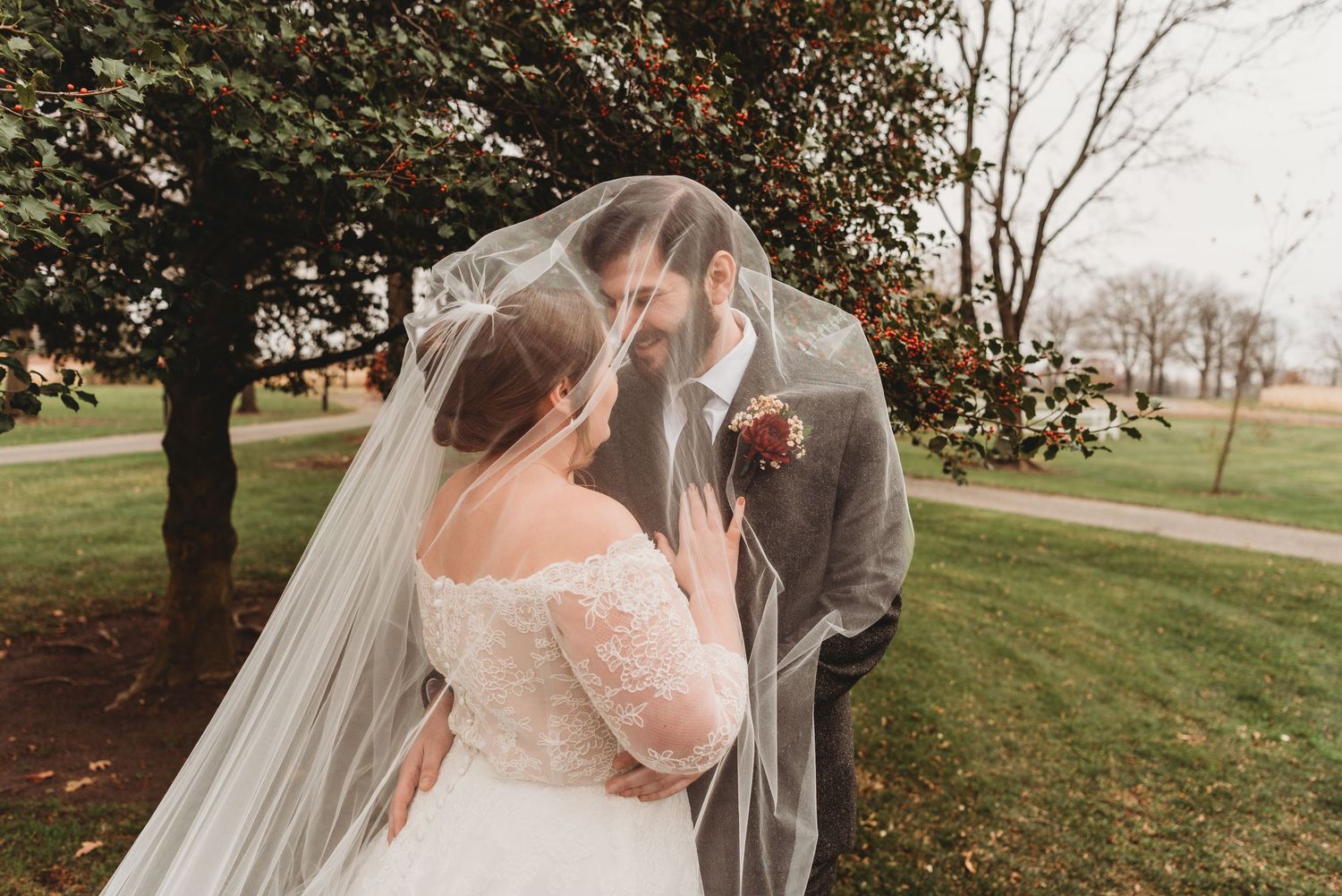 A bride and groom sharing an intimate moment under a flowing veil outdoors during their fall wedding day.