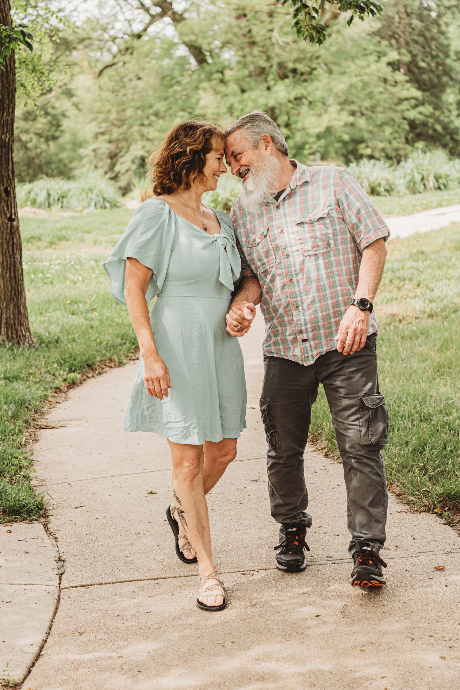 An older couple walking forehead-to-forehead on a park path, woman in mint dress holding hands.
