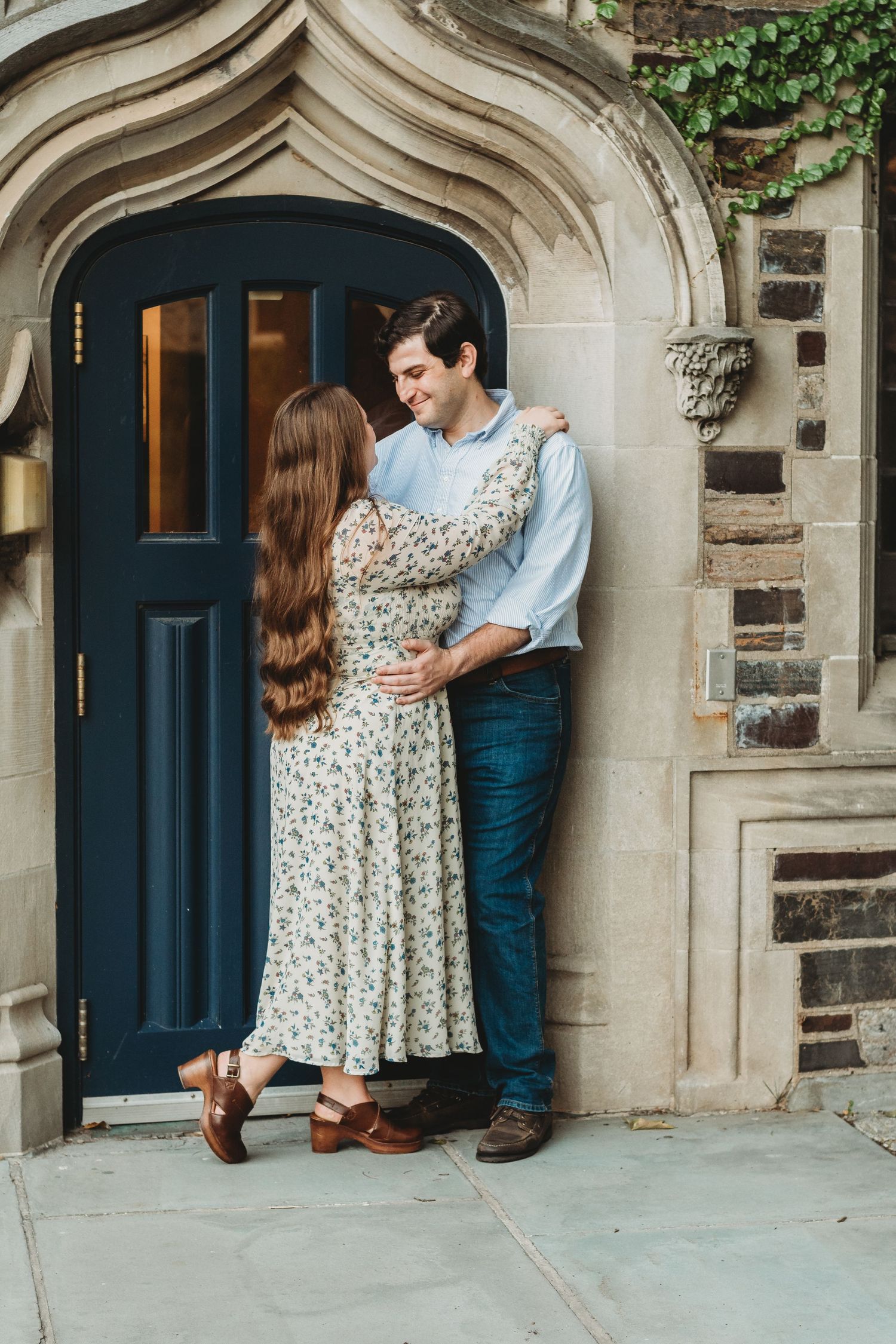 A couple embraces tenderly in front of an elegant stone archway with a navy blue door.
