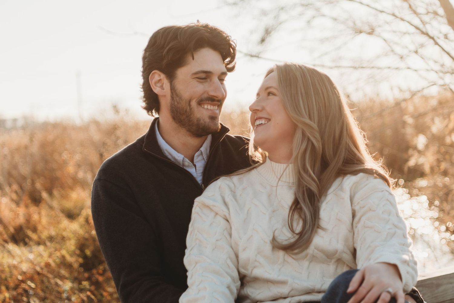 Happy couple smiling at each other during golden hour in autumn outdoor setting.