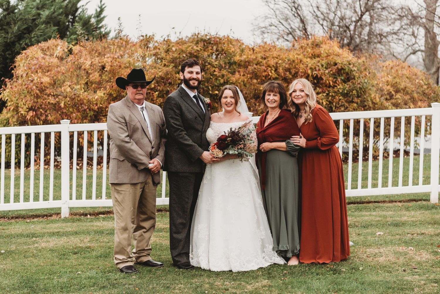 Wedding couple posing outdoors with family members in autumn foliage background.