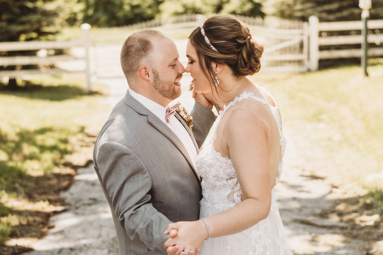 Bride and groom share romantic forehead touch in sunny outdoor wedding portrait.