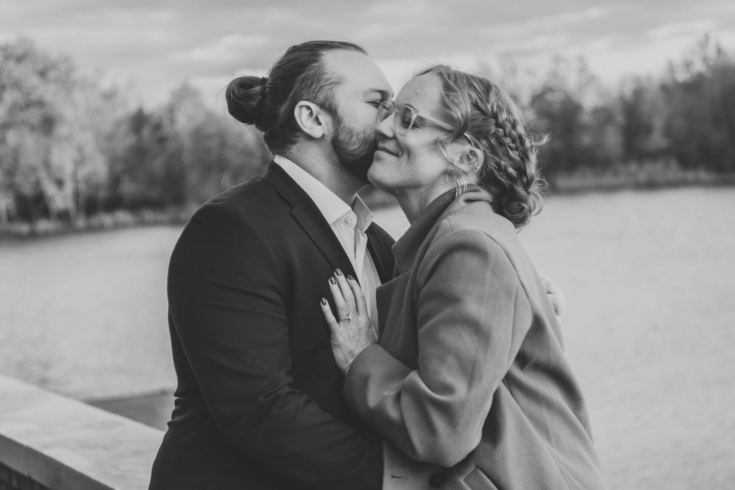 Black and white photo of couple sharing a kiss near lake.