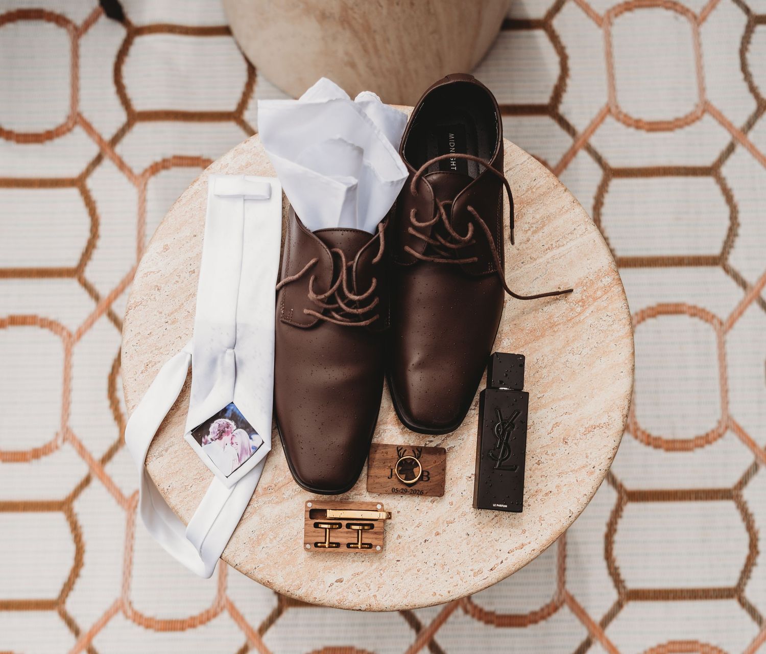 Groom wedding flat lay with brown leather shoes, white tie, gold cufflinks, and a wooden lighter.