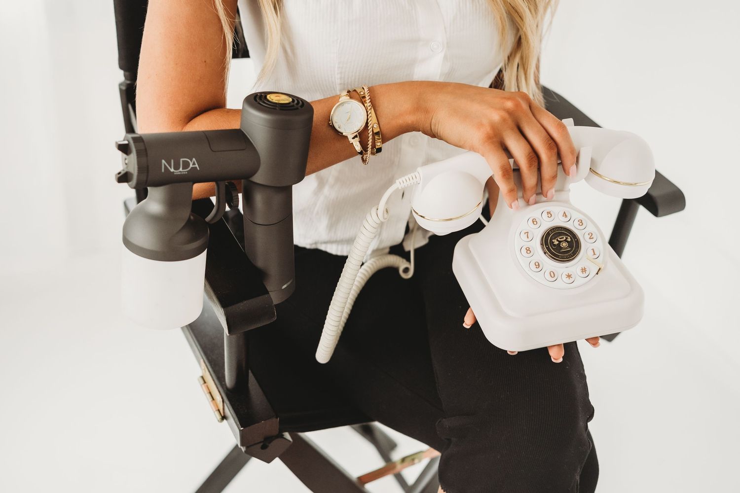 Blonde woman in white top holding vintage rotary phone beside NUDA hair dryer.