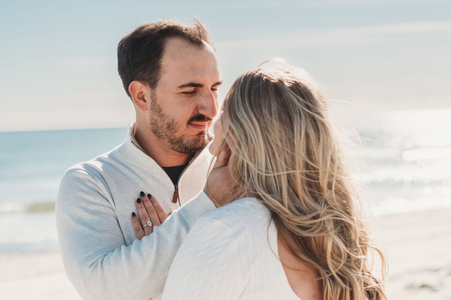 Romantic couple almost kissing on beach with ocean backdrop.