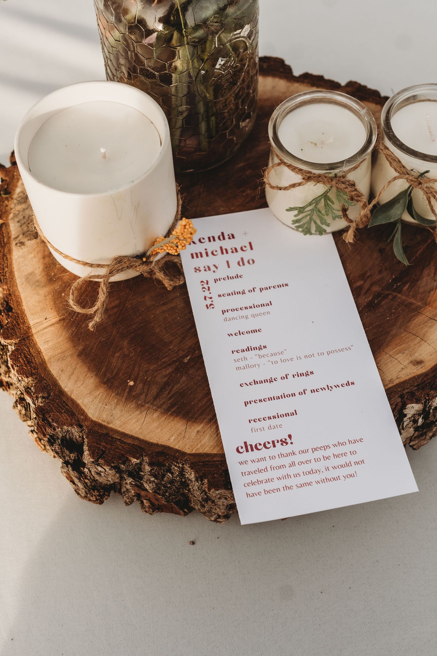 Rustic wedding ceremony program on wood slice with candles and floral decor.