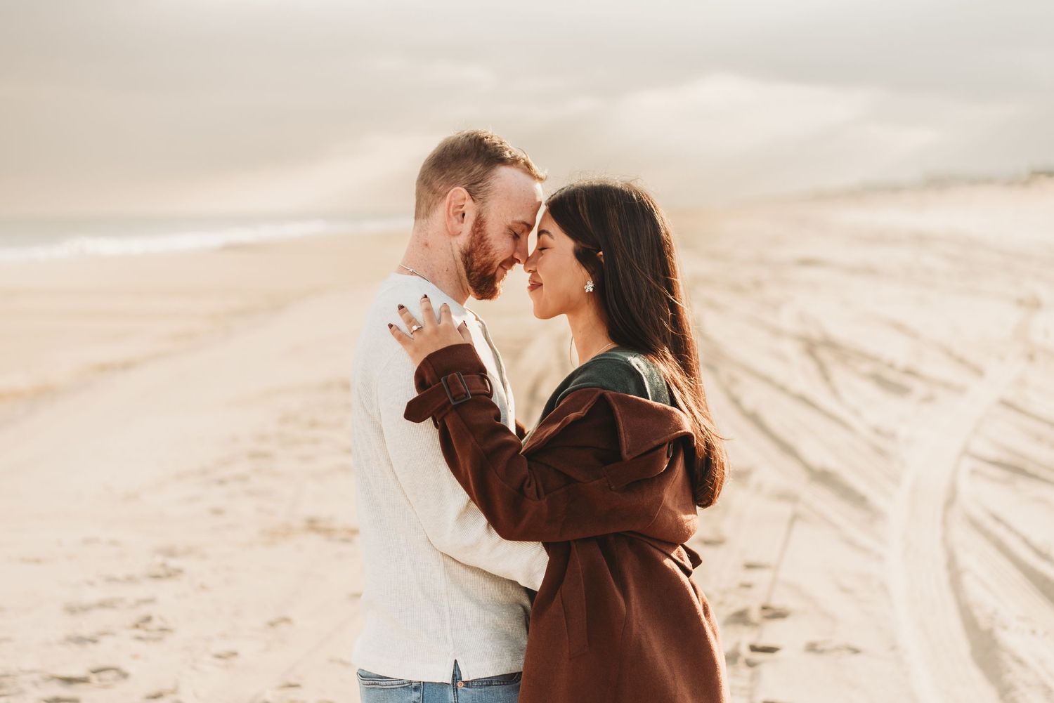 Couple embracing on sandy beach at golden hour in warm romantic setting.