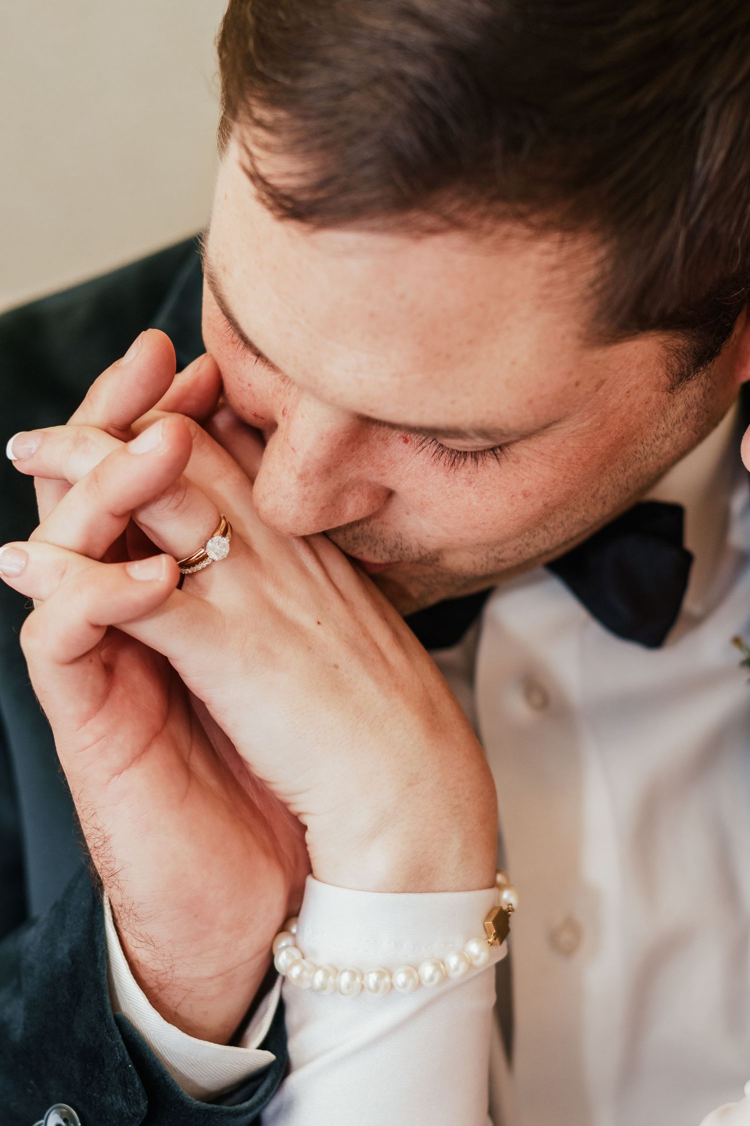 Groom tenderly kisses bride's hand adorned with pearl bracelet and engagement ring.