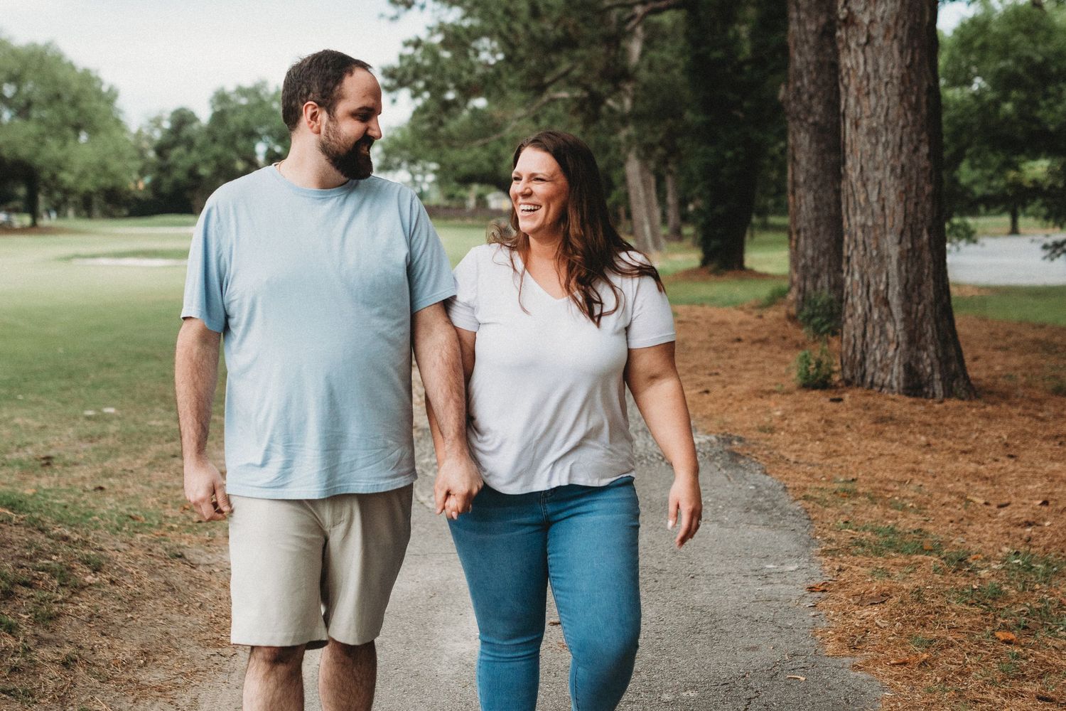 Smiling couple walking hand in hand along a tree-lined path during an outdoor photo session.