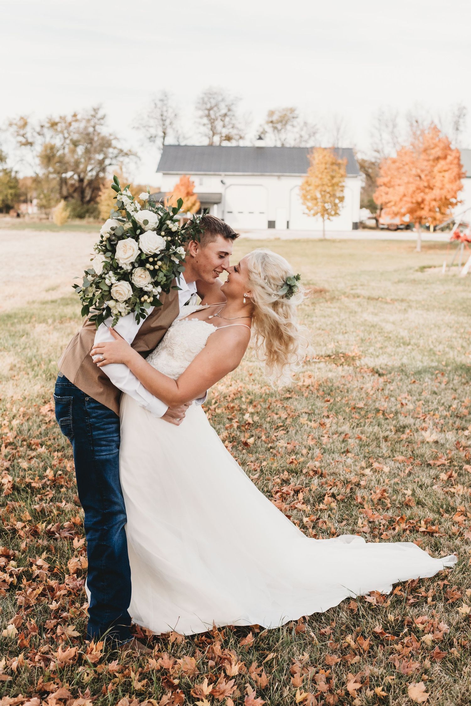 Groom dipping bride in a romantic kiss surrounded by colorful autumn leaves on their wedding day.