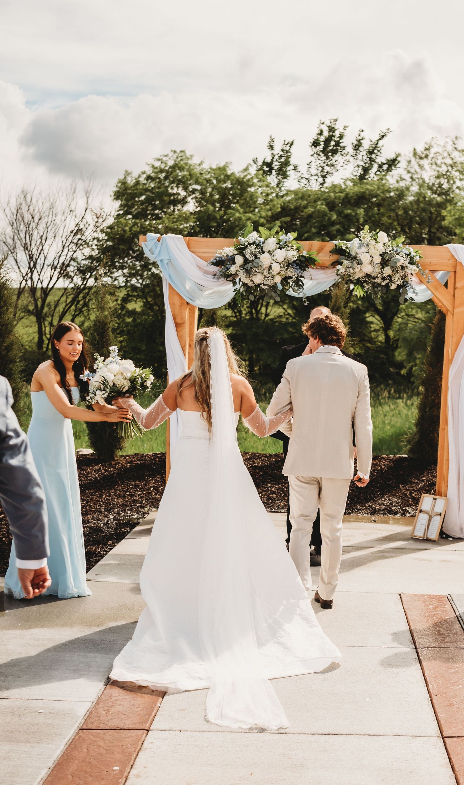 Bride and groom walking hand in hand toward a floral wooden arch at outdoor wedding ceremony.