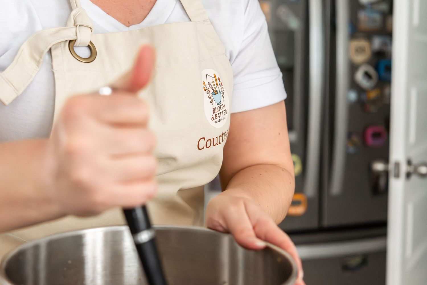 Person in Courtney apron stirring mixture in large metal pot in kitchen.