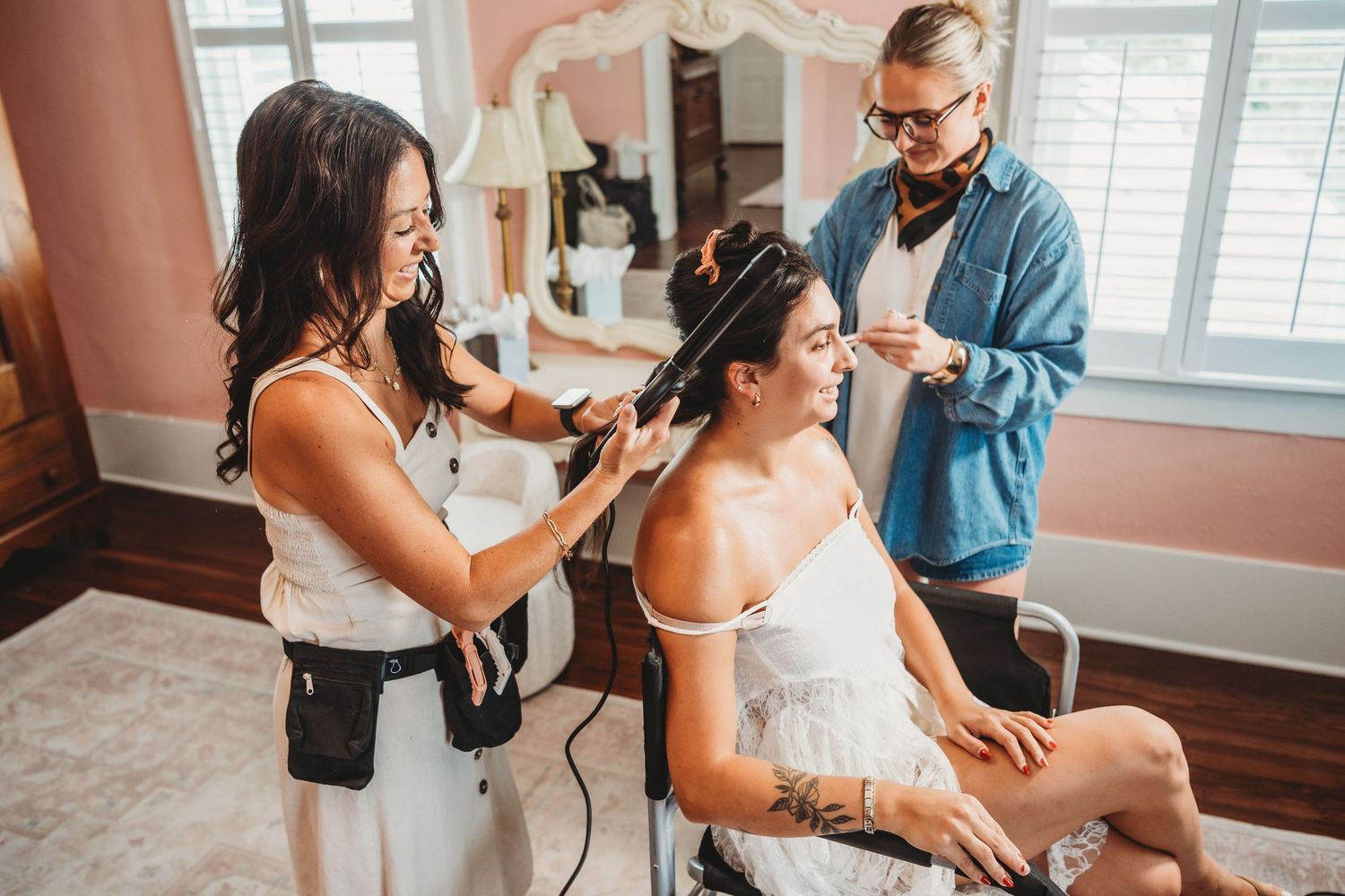 Hair stylist curling seated womans hair while male assistant helps in pink salon.