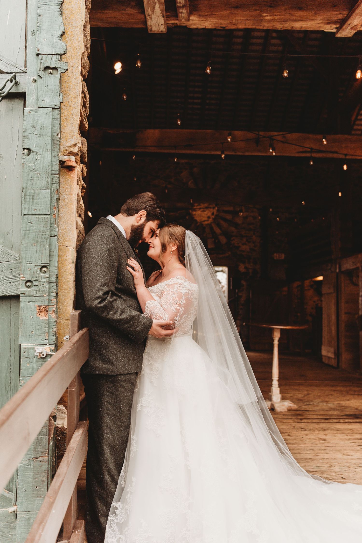 Bride and groom sharing an intimate moment in a rustic barn doorway, veil trailing behind her.