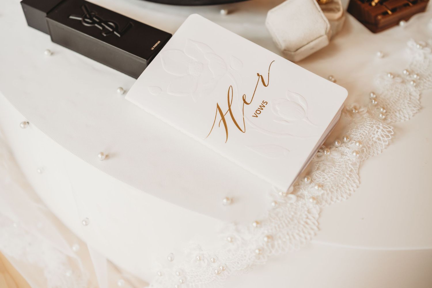 Elegant white wedding vow book with gold Her script lettering on a lace bridal accessory.