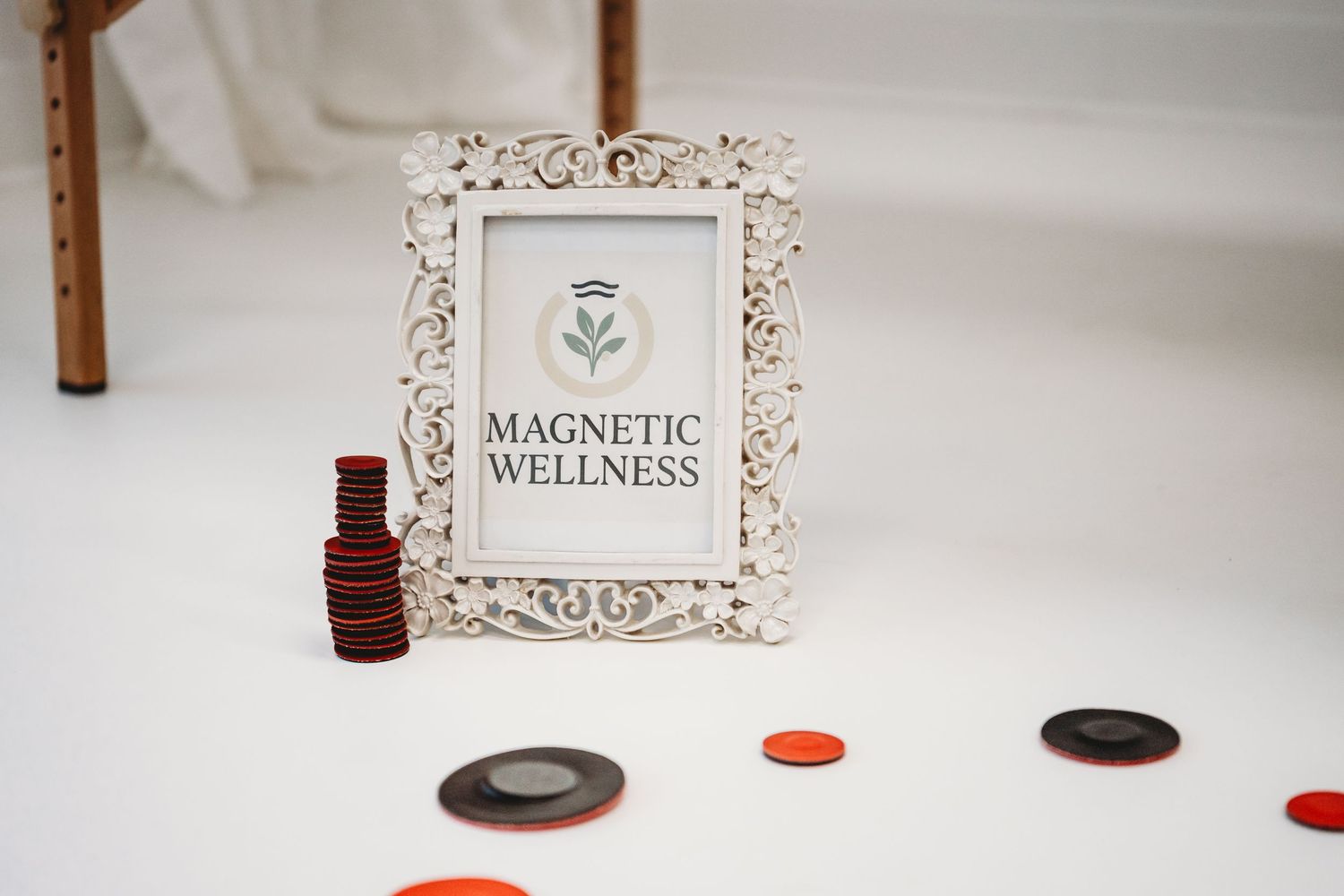 White ornate frame displaying Magnetic Wellness logo surrounded by red and black magnetic discs on white surface.