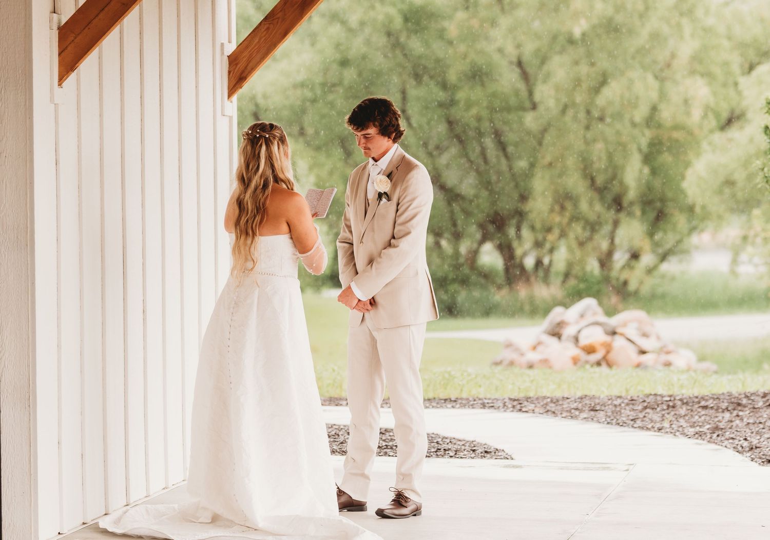 Bride and groom holding hands during intimate first look outside a white barn wedding venue.